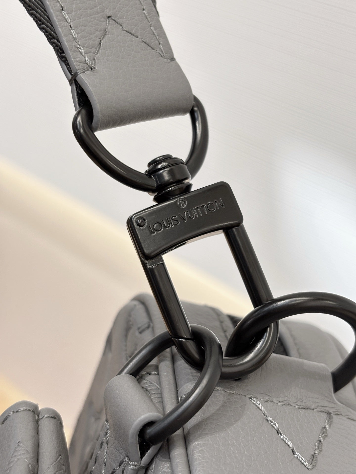 Louis Vuitton gray strap with keyring and logo tag attached to crossbody bag hardware