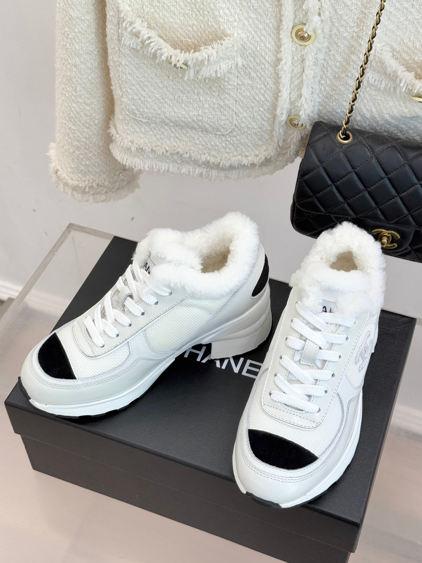White sneakers with black toe accents and fluffy fur-lined cuffs on a box