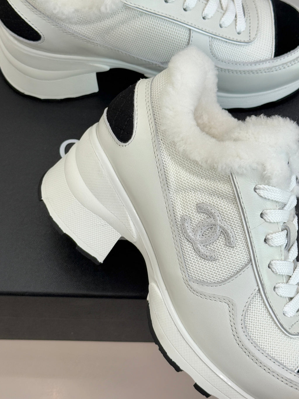 Close-up of white sneaker with textured panel, black side insert, and fur lining