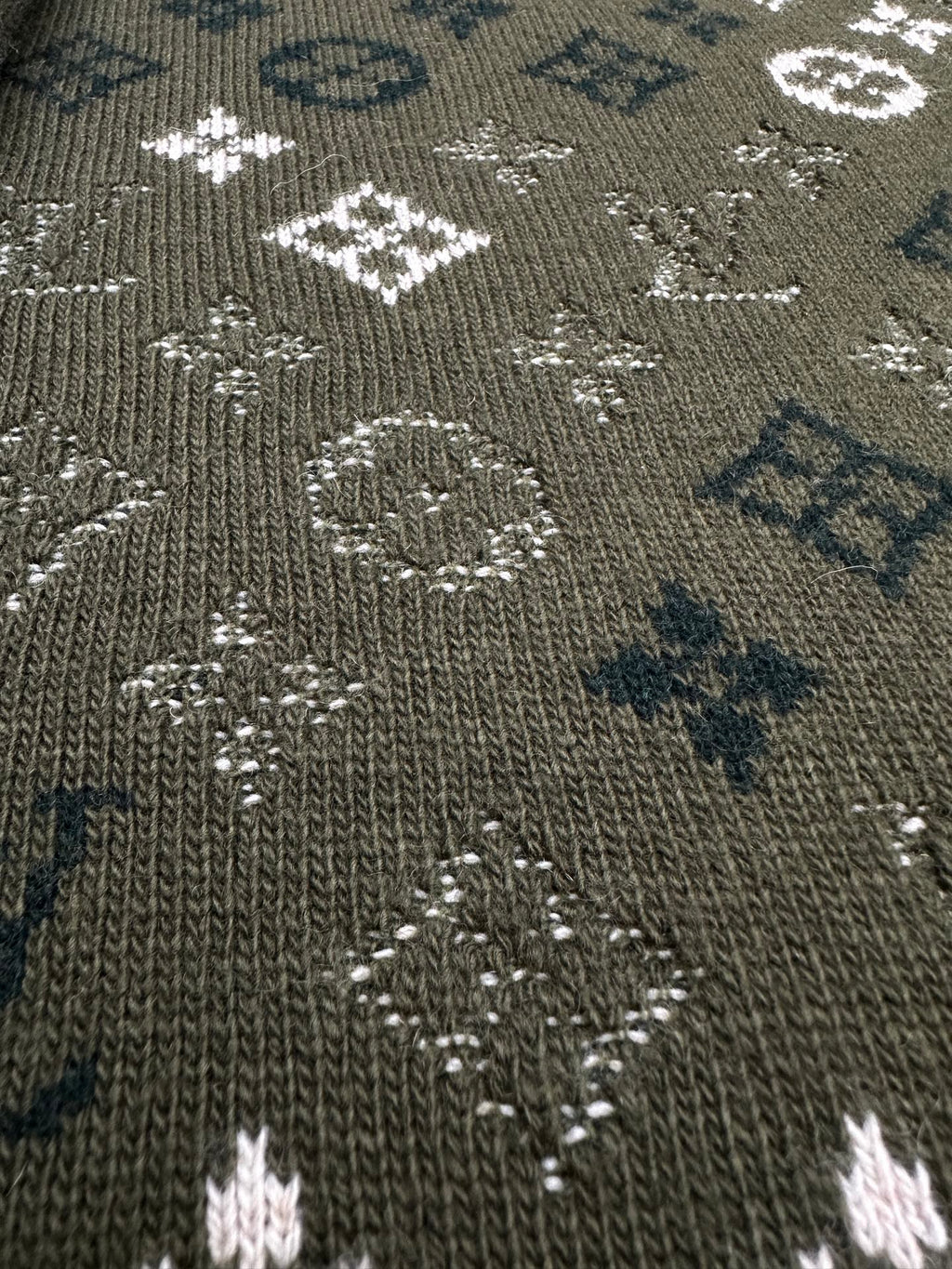 Close-up of dark green knit sweater fabric with dotted white and blue logo pattern