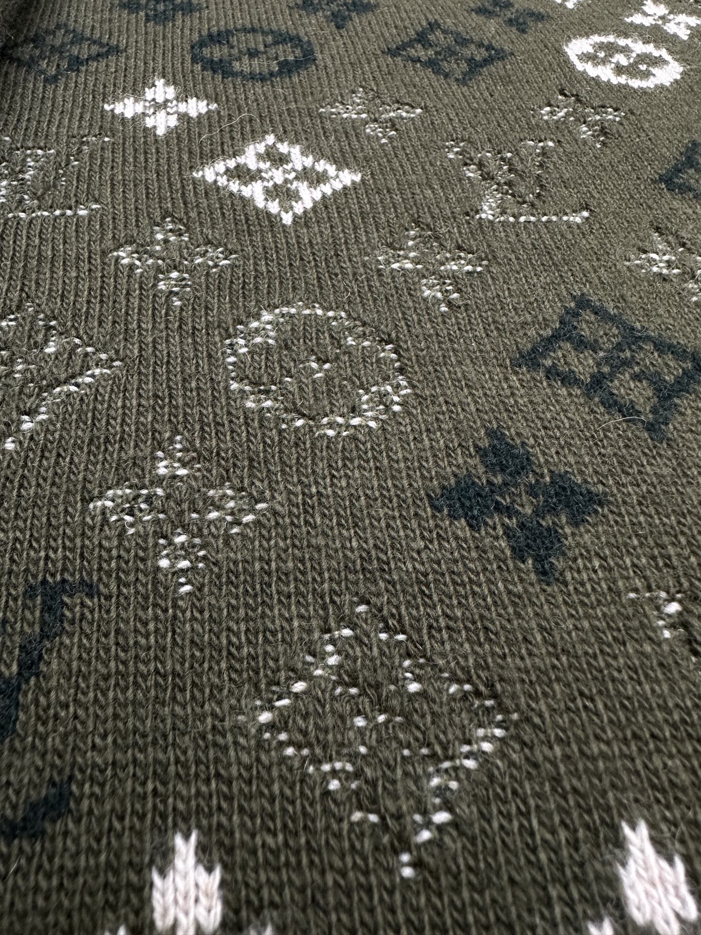 Close-up of dark green knit sweater fabric with dotted white and blue logo pattern