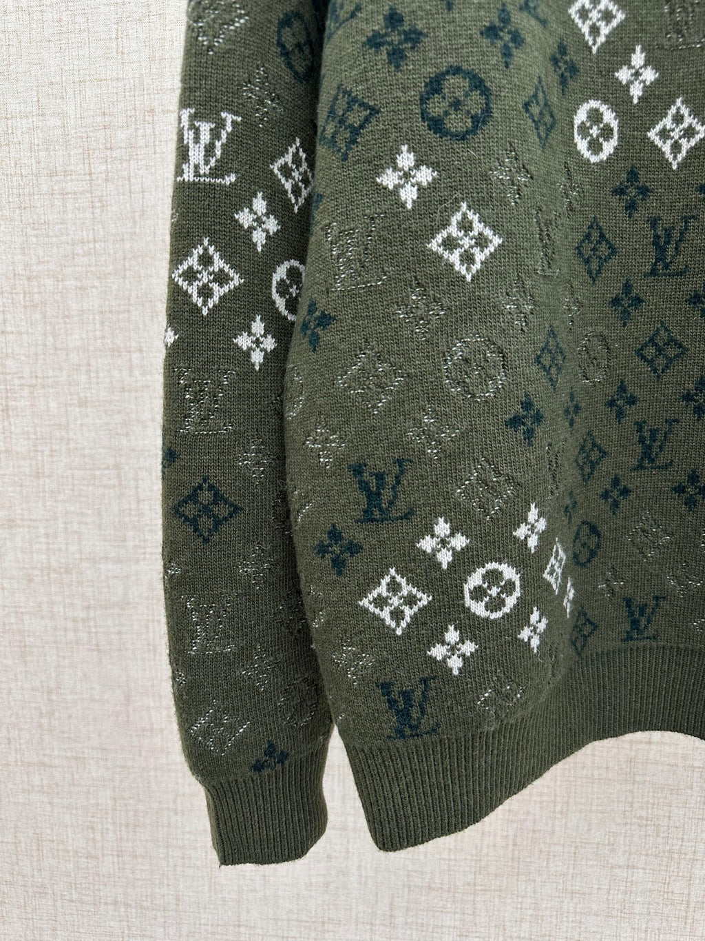 Dark green knit sweater sleeve with all-over logo pattern and ribbed cuff