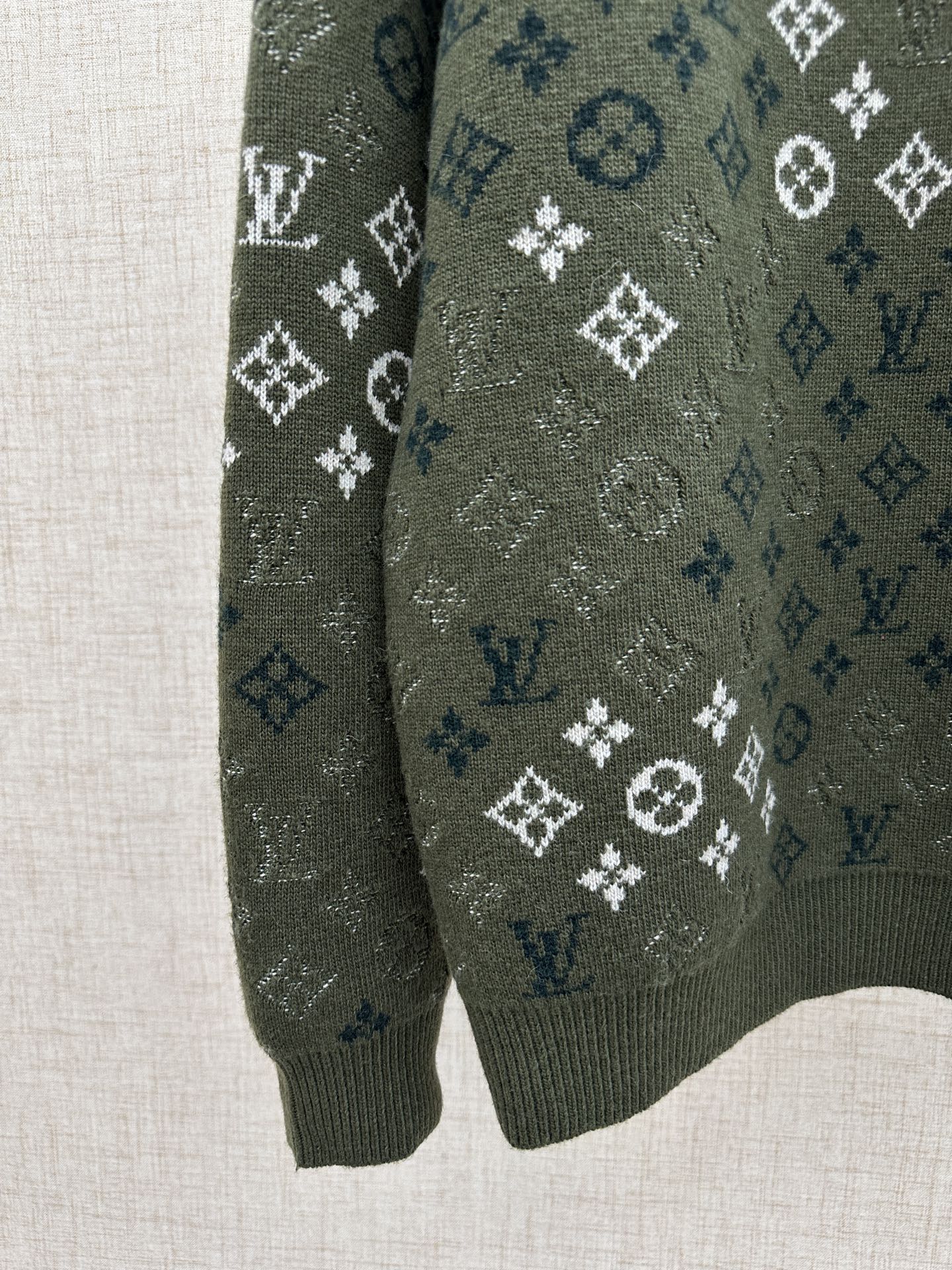 Dark green knit sweater sleeve with all-over logo pattern and ribbed cuff