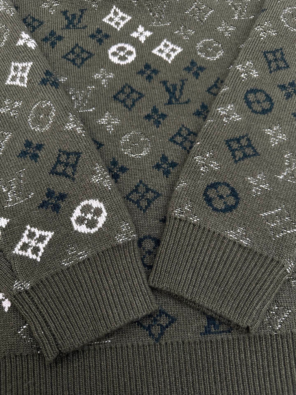 Close-up of dark green knit sweater cuffs with white and blue logo monogram pattern