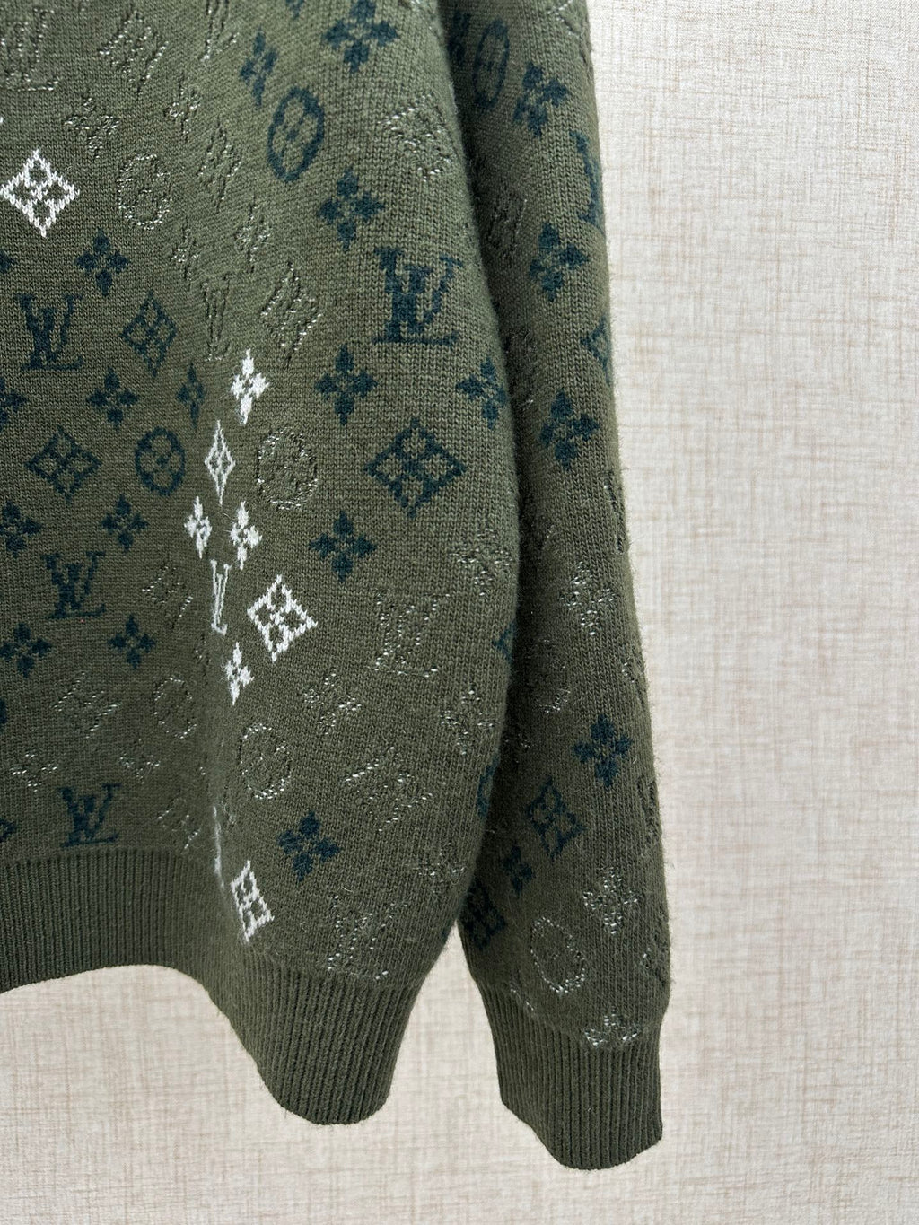 Dark green knit sweater sleeve and hem with white and blue logo monogram pattern