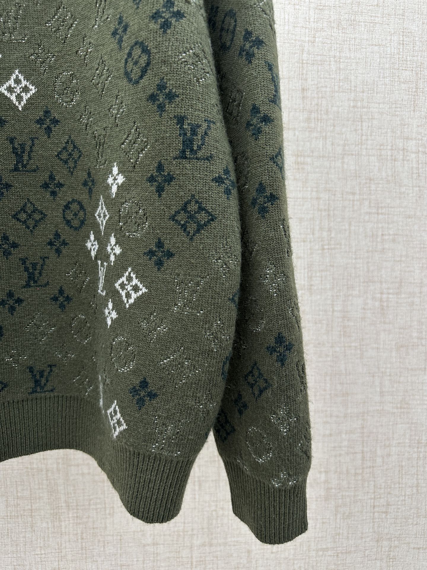 Dark green knit sweater sleeve and hem with white and blue logo monogram pattern
