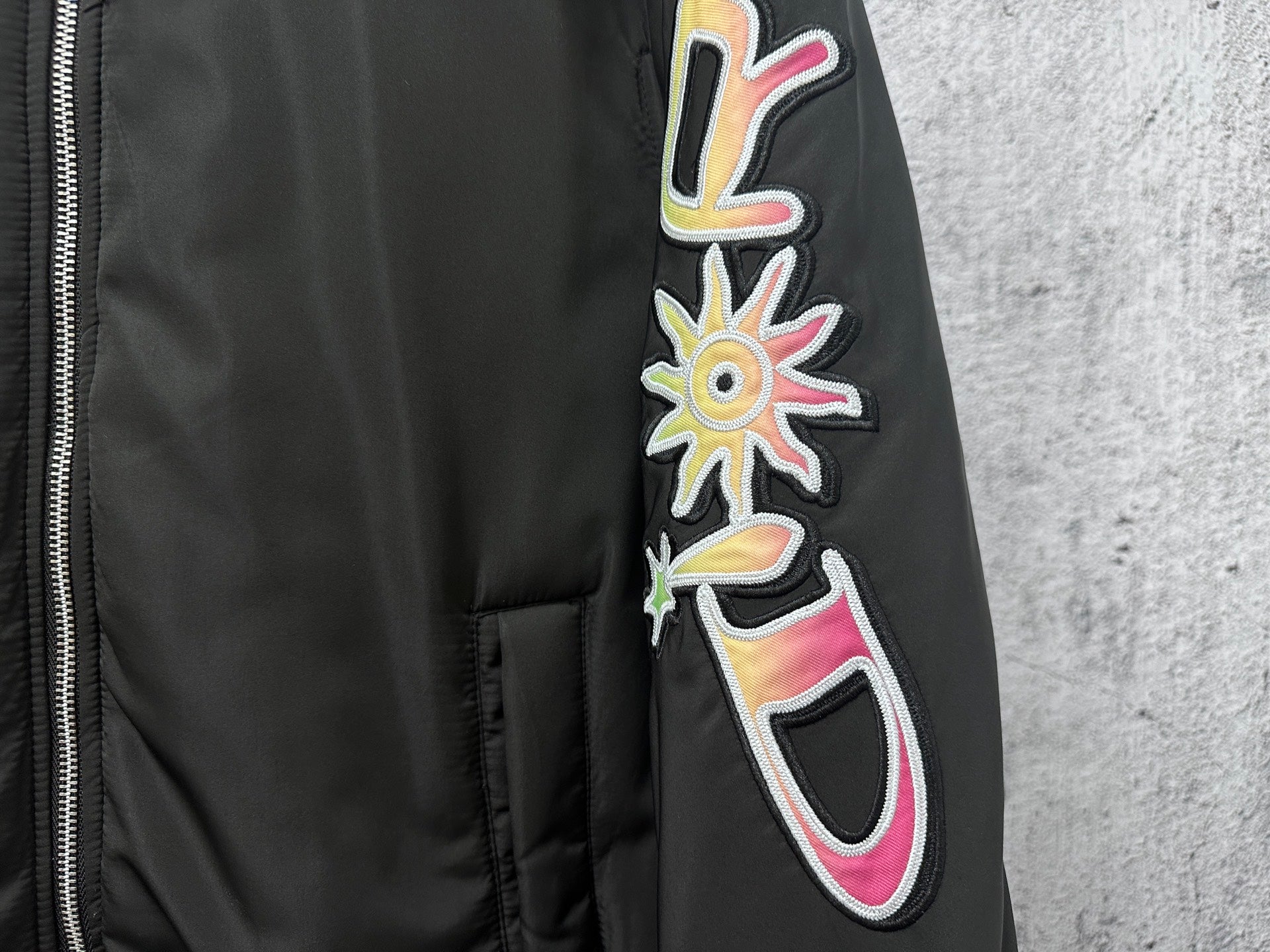 Dior black bomber jacket sleeve graphic patch with colorful flower and swirl details