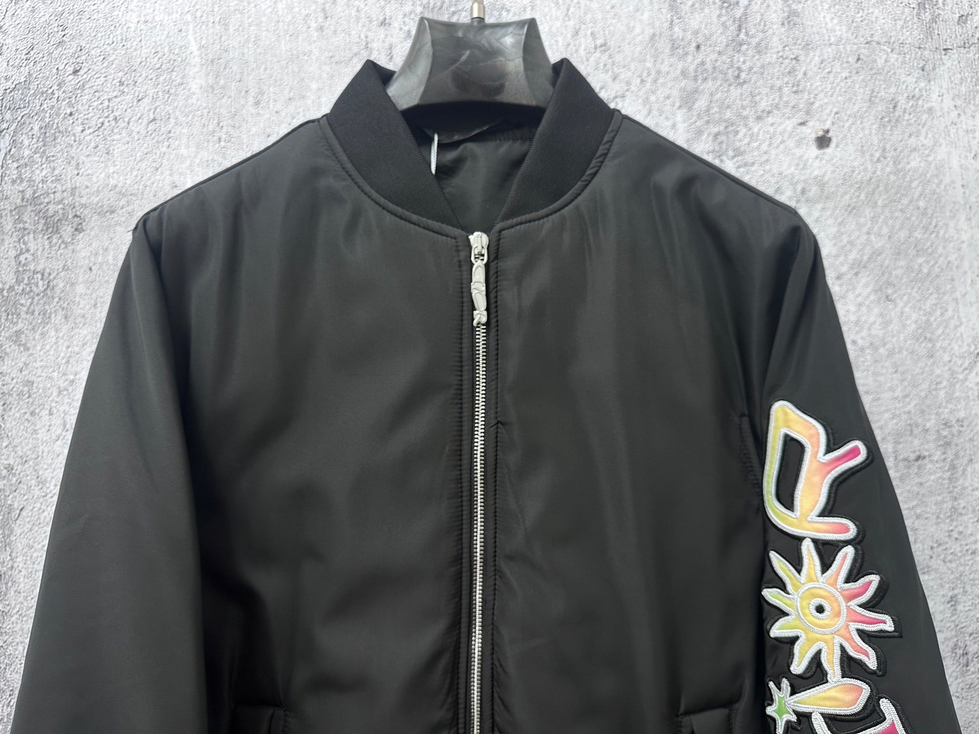 Dior black bomber jacket front with zip, pink stripe accents, flower-and-47 sleeve graphic