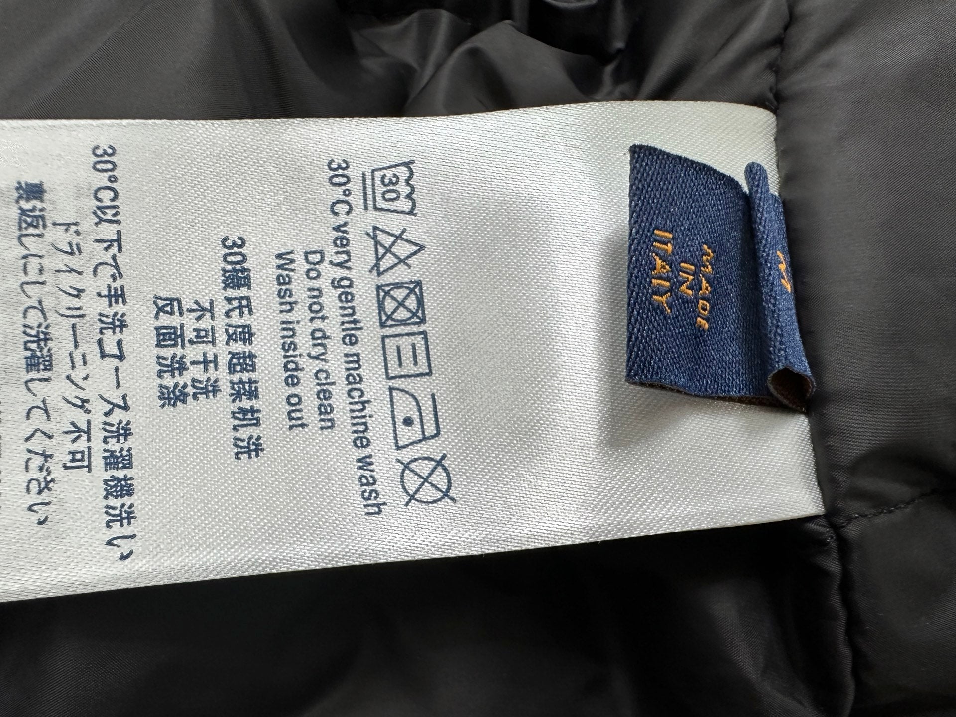 Jacket care label with fabric instructions and brand tag attached inside collar