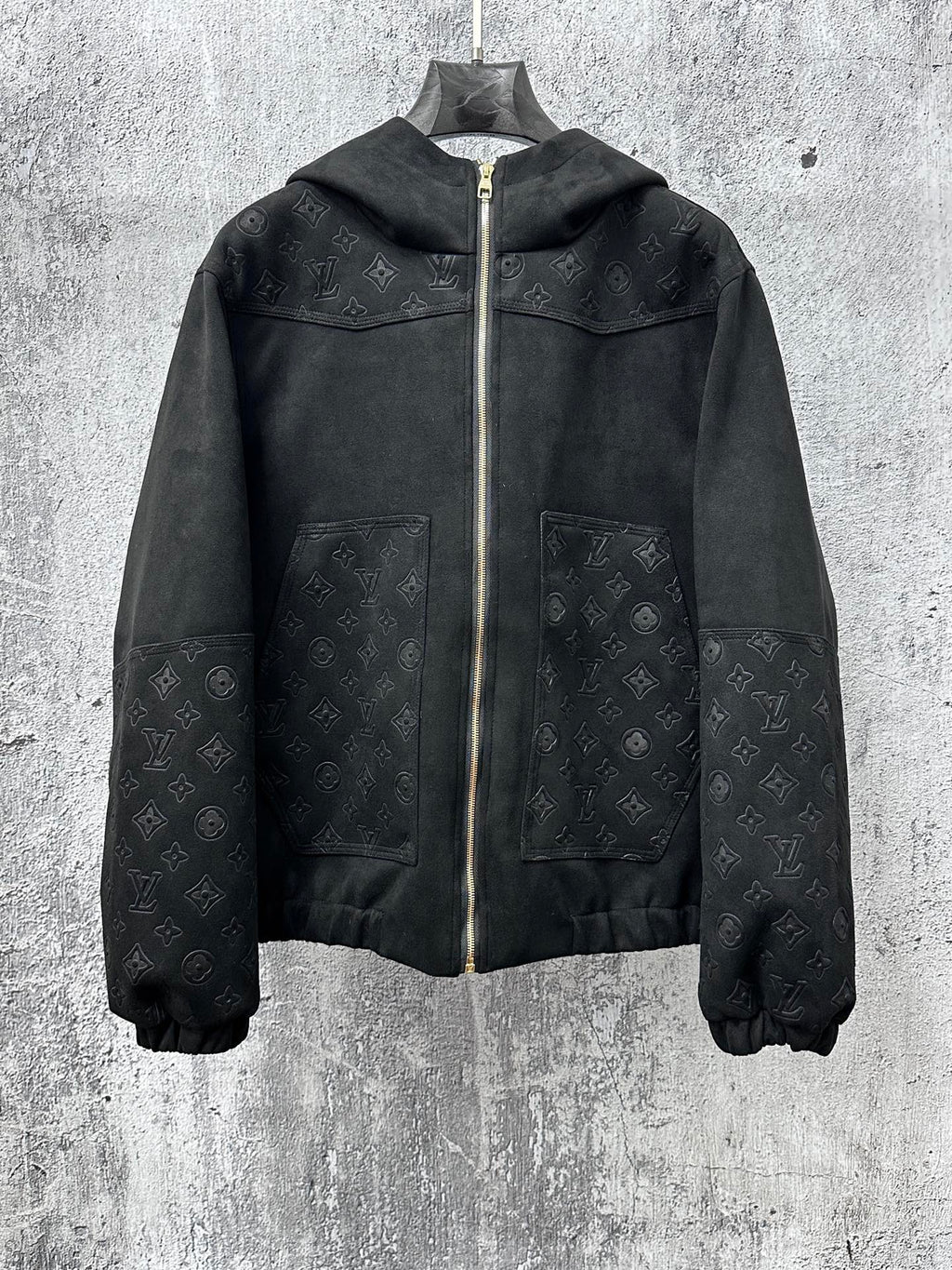 Dark hooded zip jacket with subtle monogram pattern and gold zipper hardware