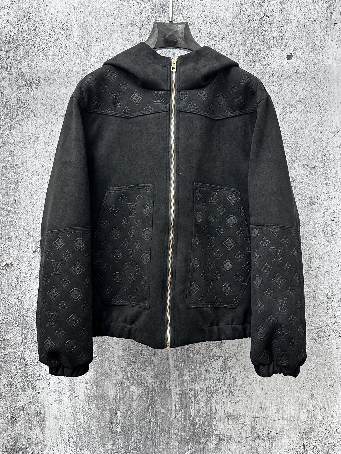 Dark hooded zip jacket with subtle monogram pattern and gold zipper hardware