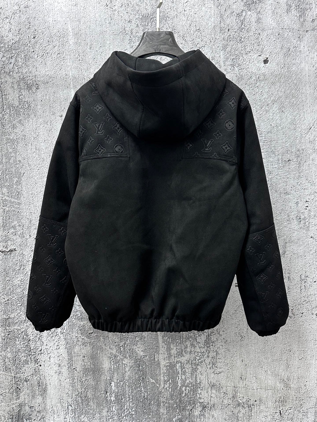 Dark hooded zip jacket with raised collar and full monogram pattern on sleeves