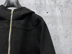 Dark hooded jacket close-up with gold-tone zipper and embossed monogram details