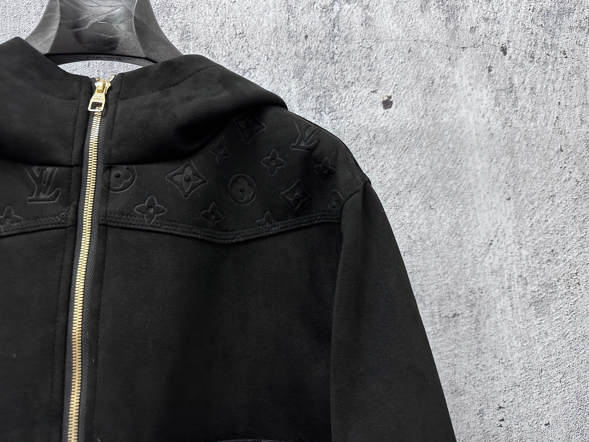 Dark hooded jacket close-up with gold-tone zipper and embossed monogram details