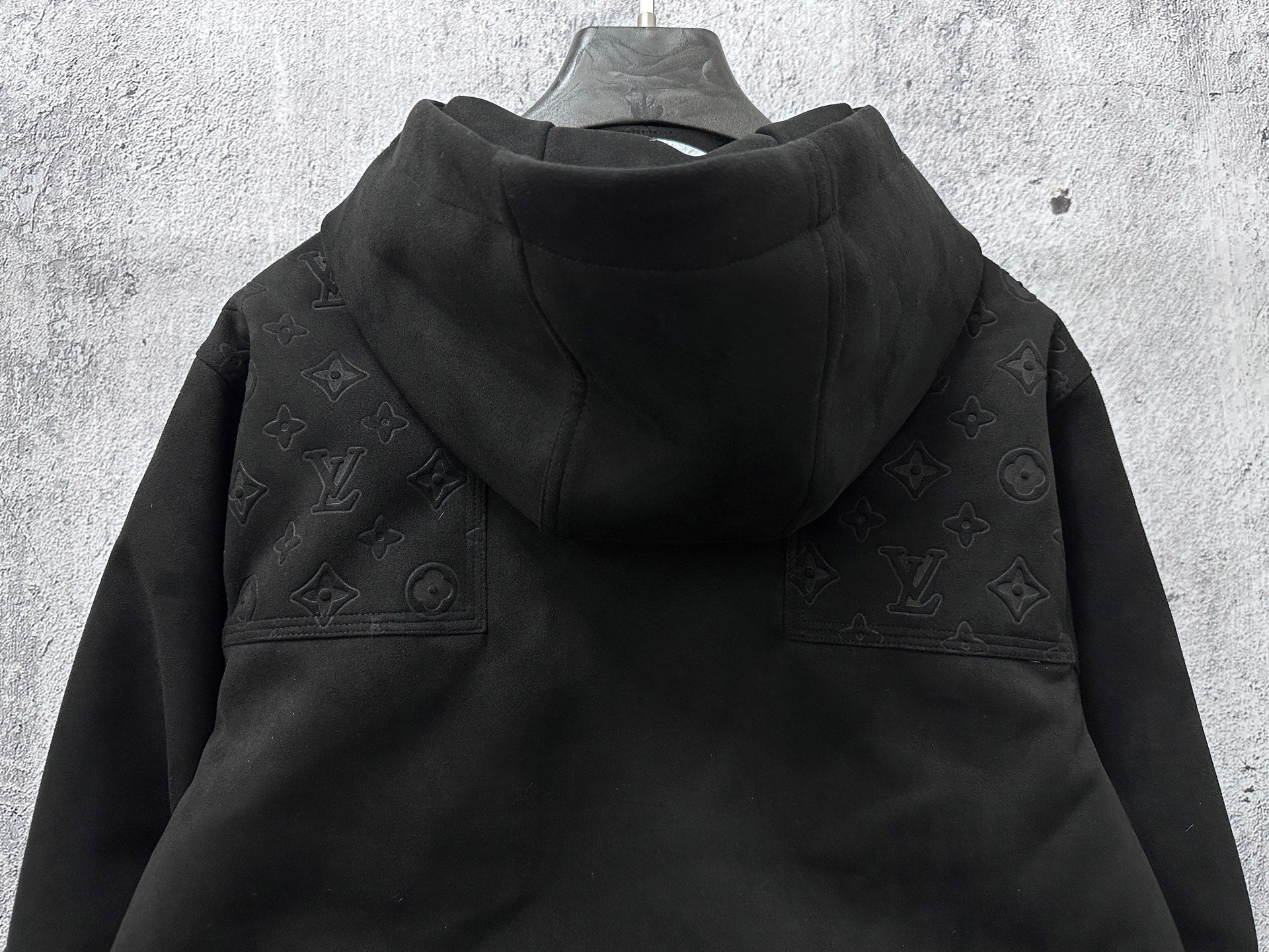 Dark hooded jacket back view with monogram shoulder panels and gathered hem