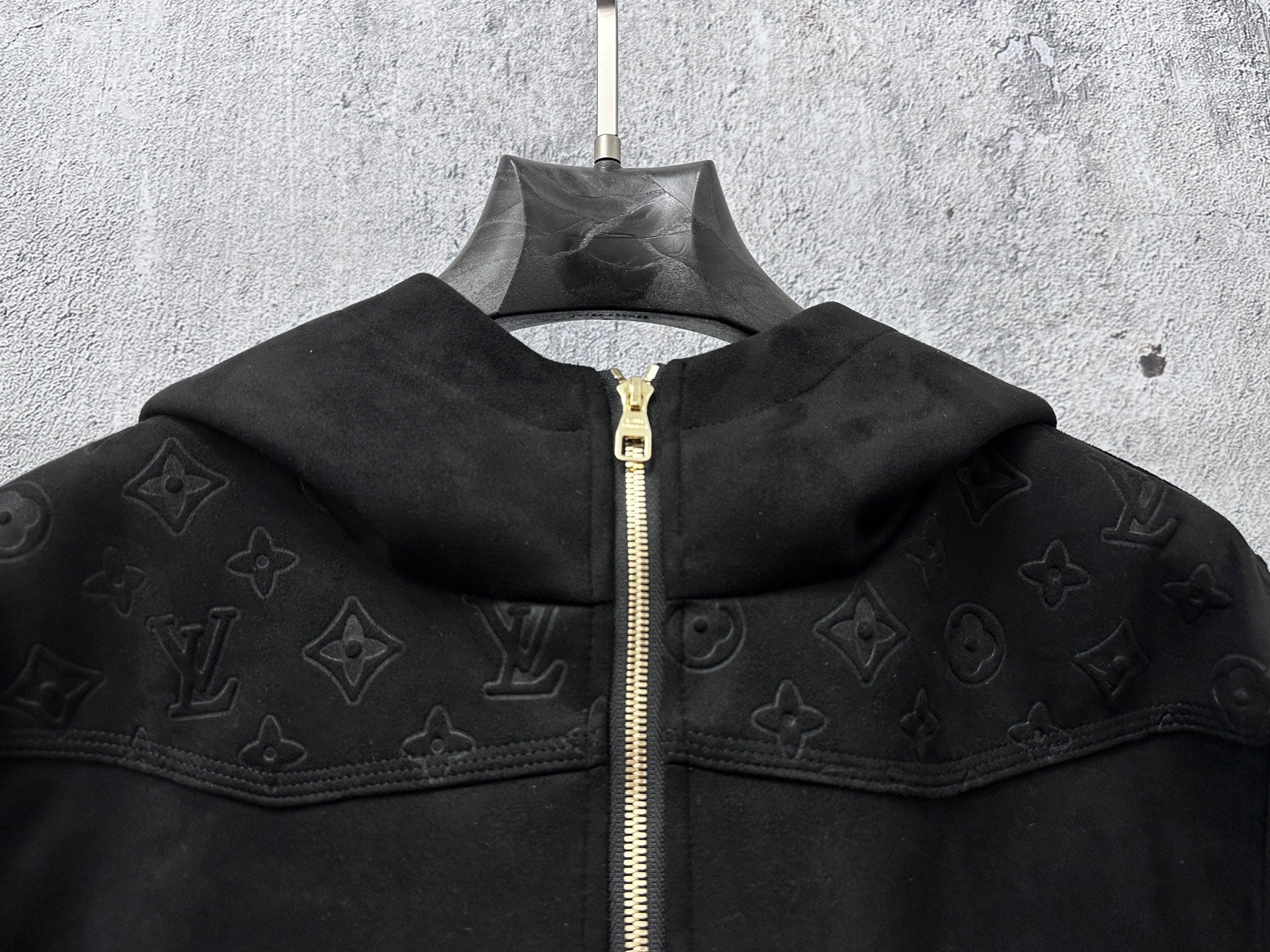 Dark hooded zip jacket close-up showing wide collar and gold zipper