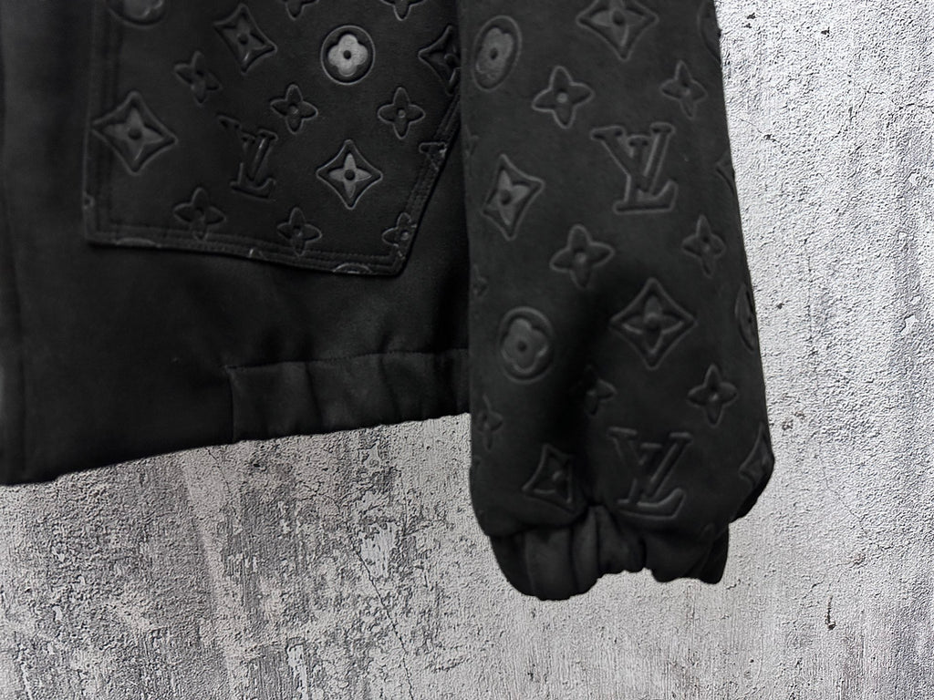 Dark jacket sleeve and hem close-up with embossed monogram pattern and cuff elastic