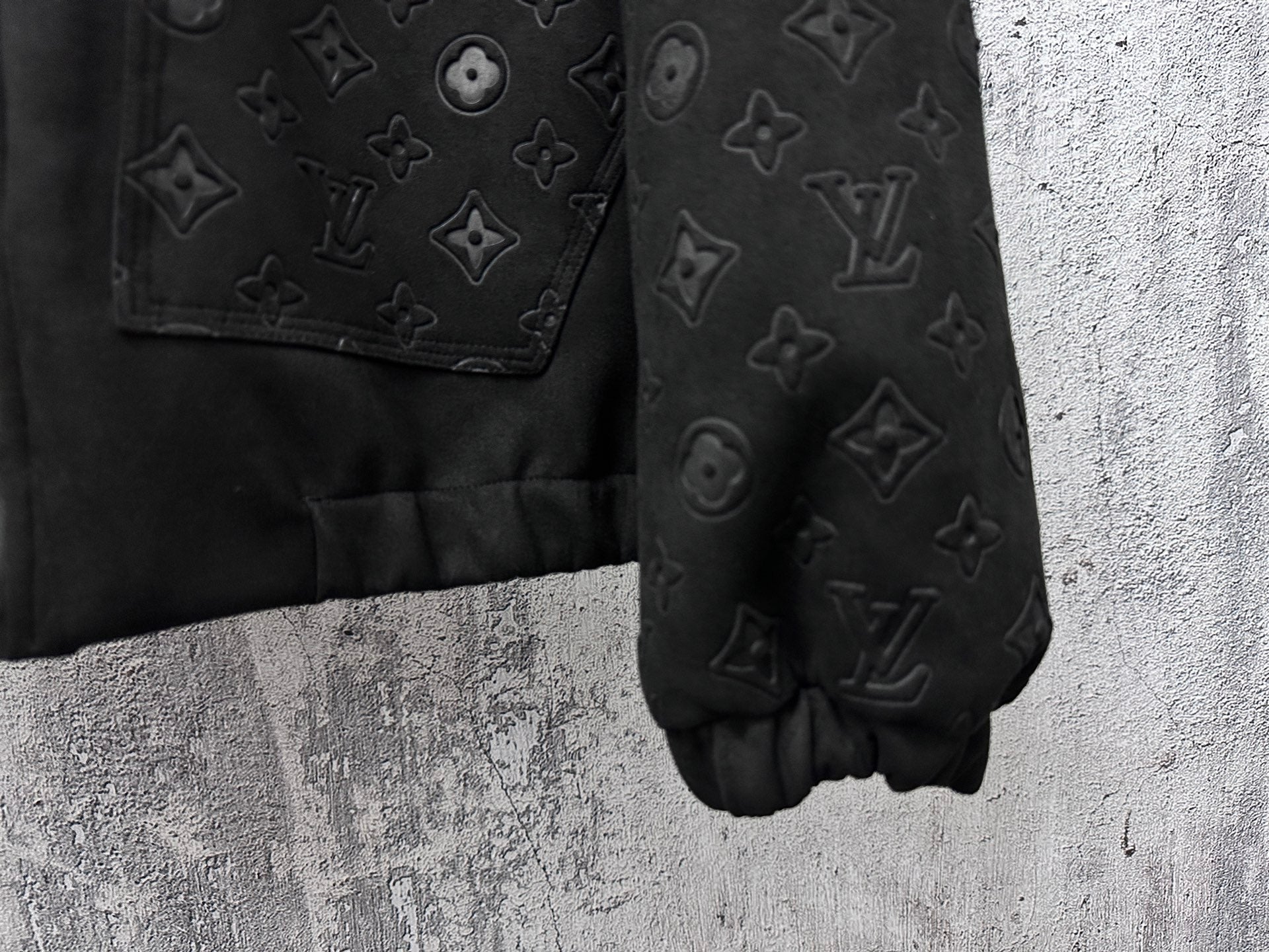 Dark jacket sleeve and hem close-up with embossed monogram pattern and cuff elastic