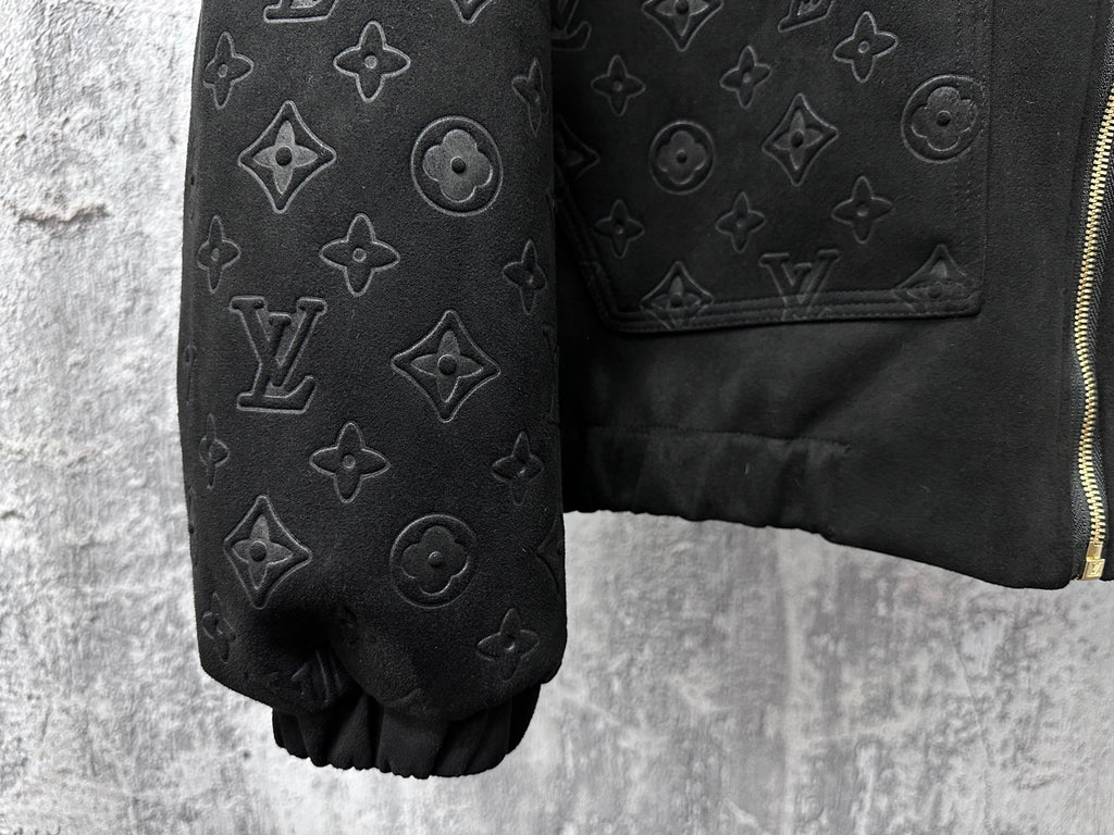 Dark sleeve close-up with embossed monogram icons and partial gold zipper
