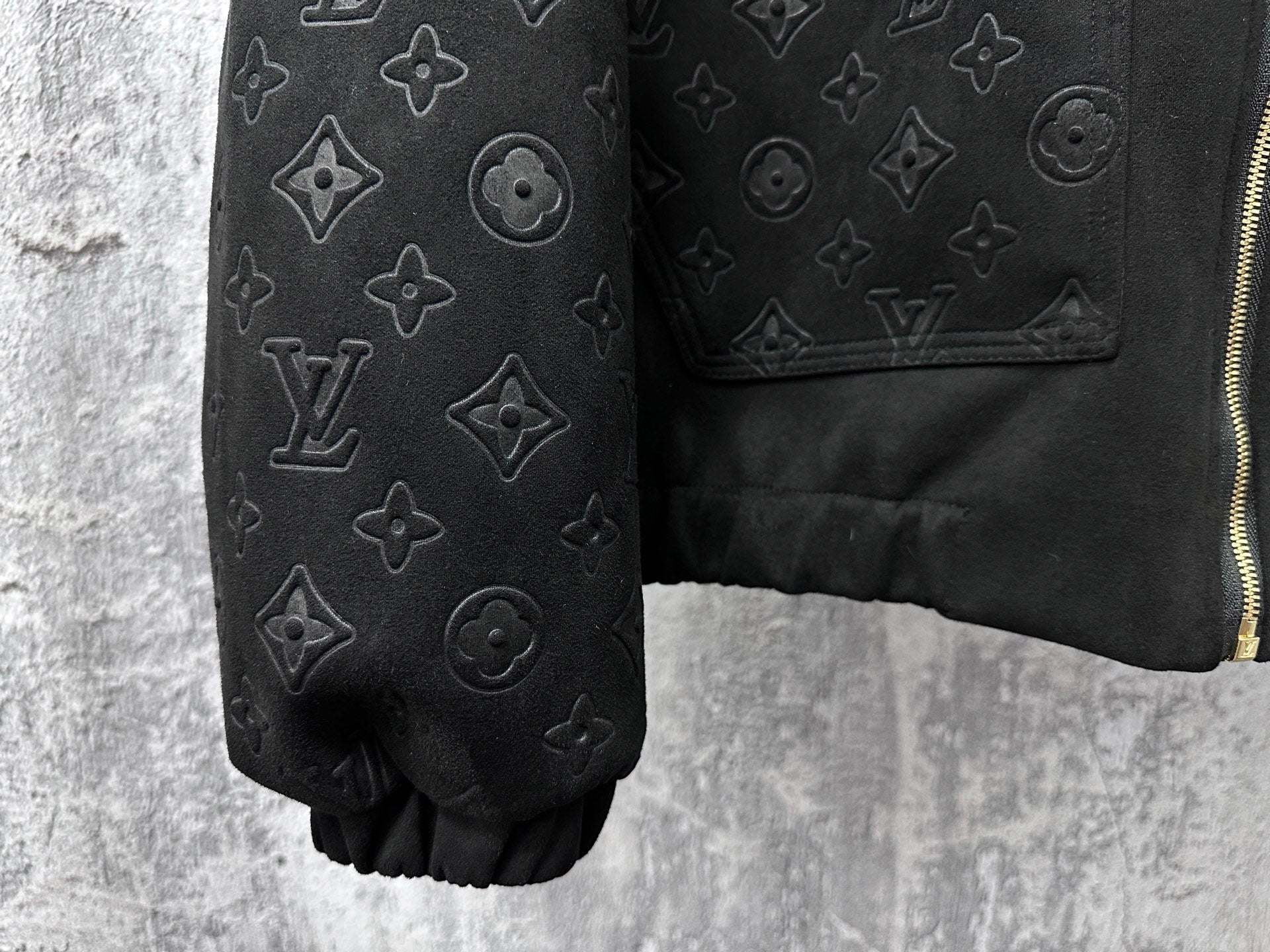 Dark sleeve close-up with embossed monogram icons and partial gold zipper
