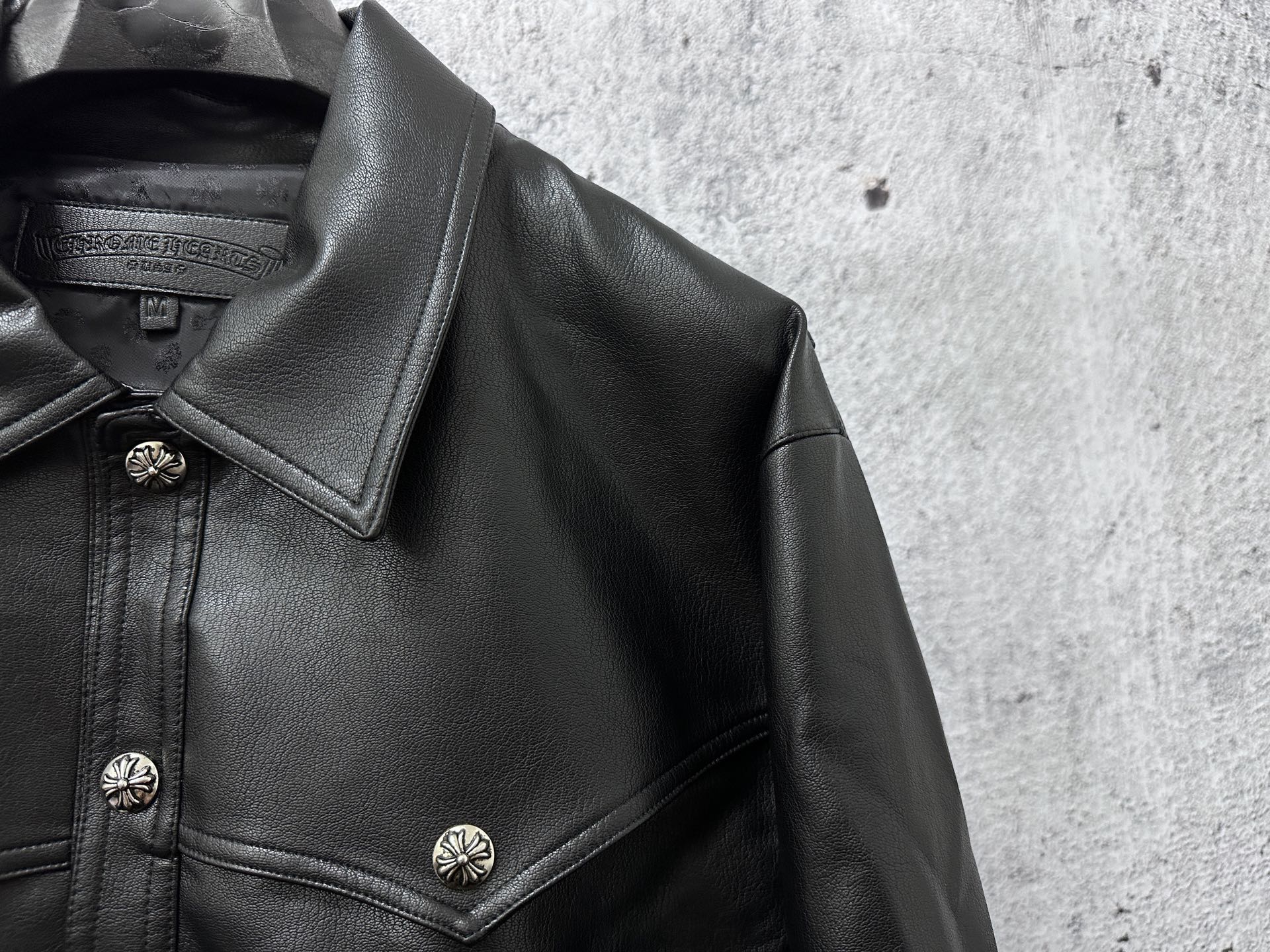 Close-up of dark leather jacket collar and shoulder with decorative snap buttons.