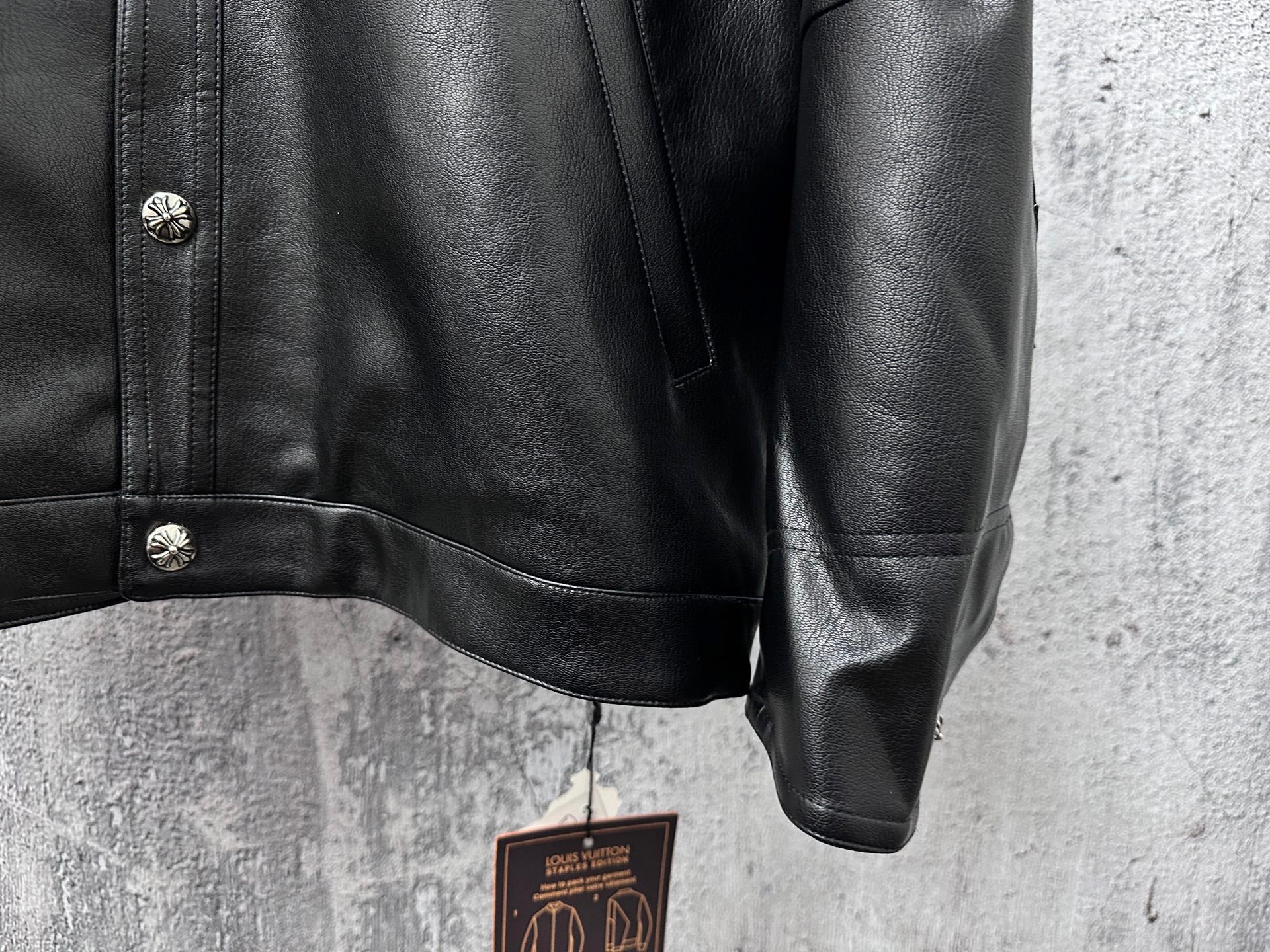 Dark leather jacket sleeve and shoulder with snap detail at cuff.