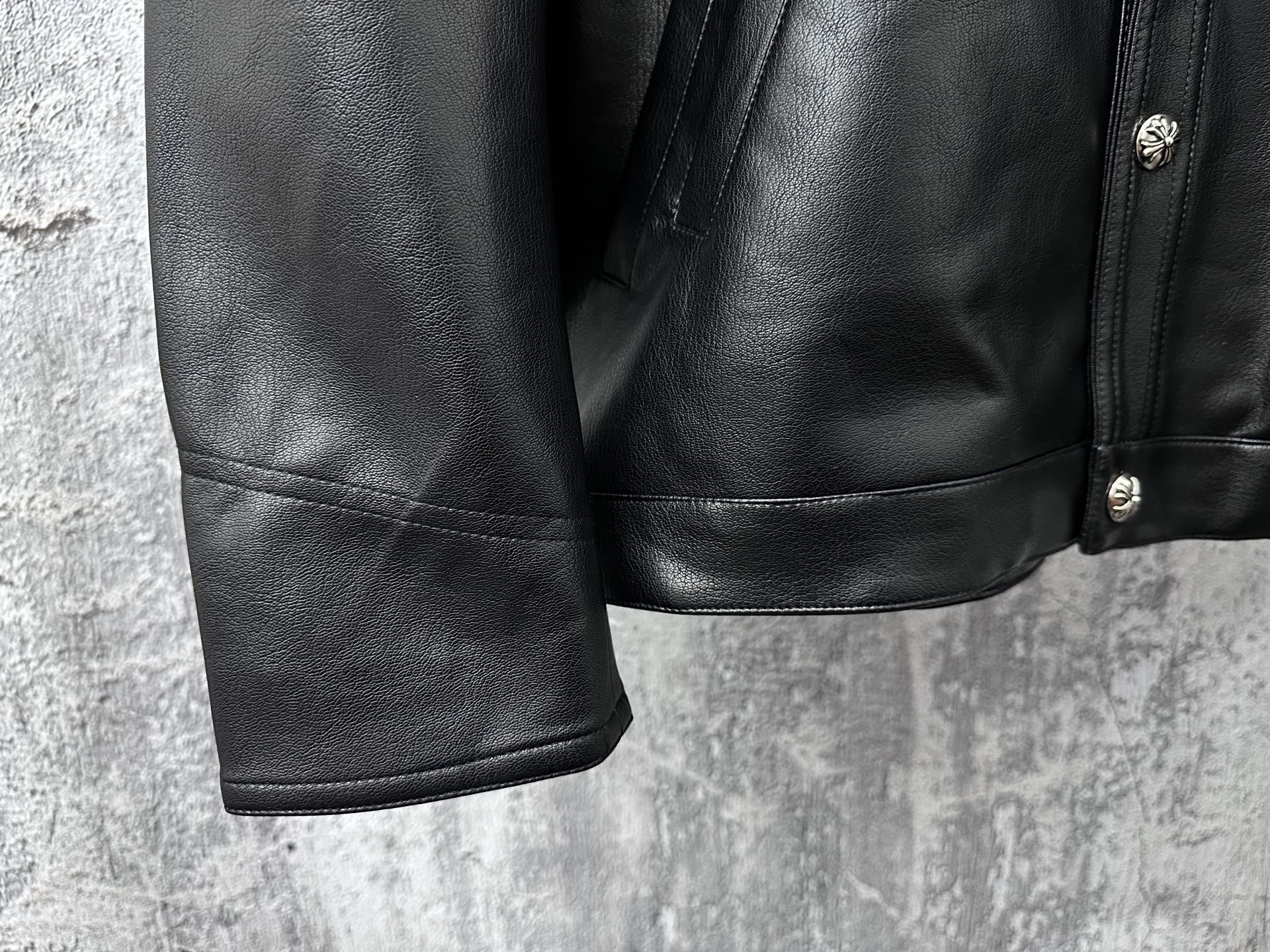 Dark leather jacket lower front with side seam paneling and buttoned detail.