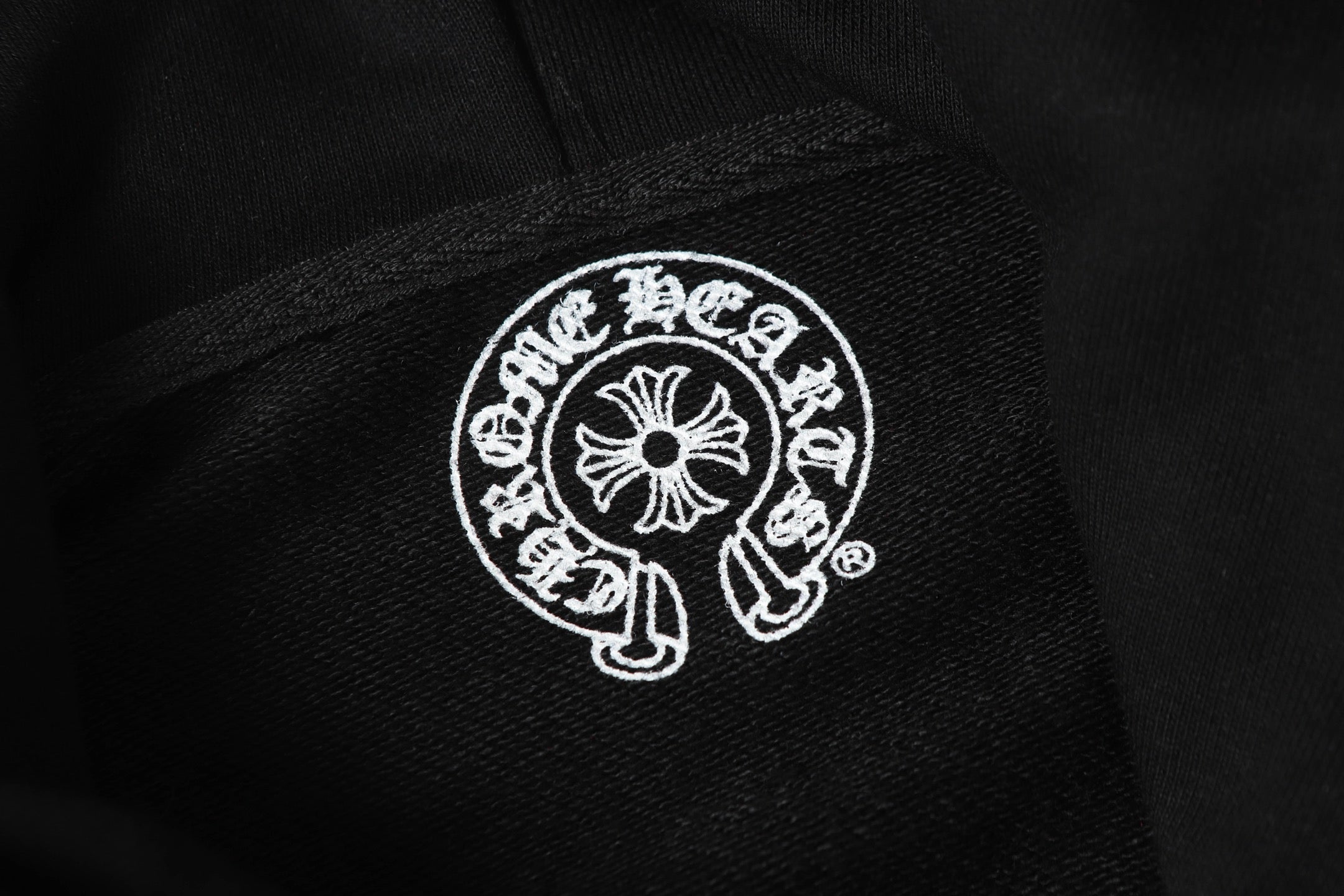 Black hoodie fabric close-up with small circular white logo