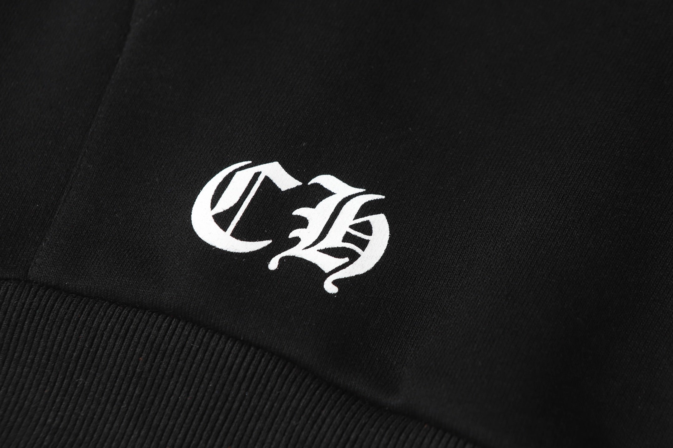 Black hoodie close-up with white monogram logo on fabric