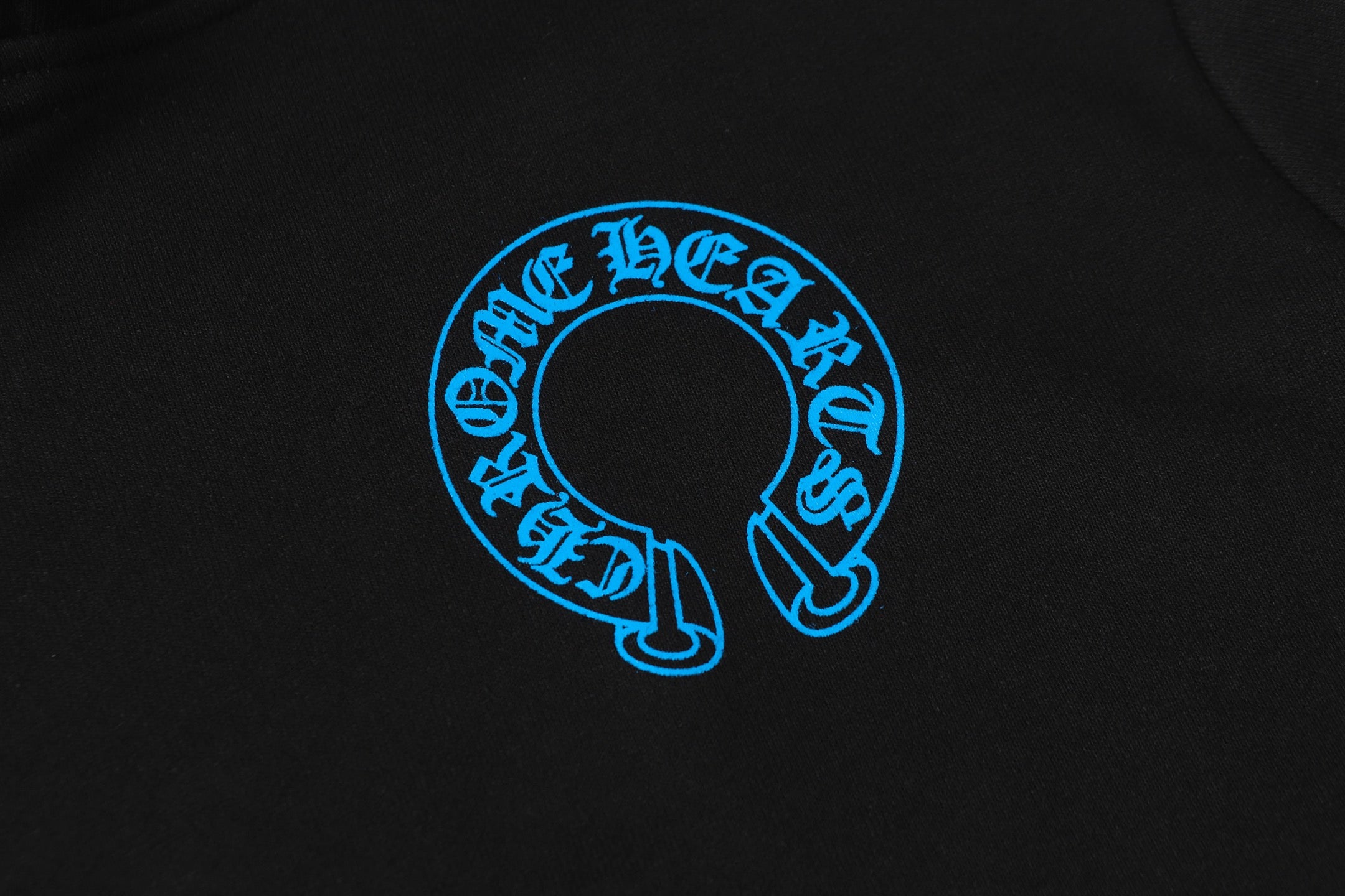 Blue circular logo emblem on black hoodie fabric close-up