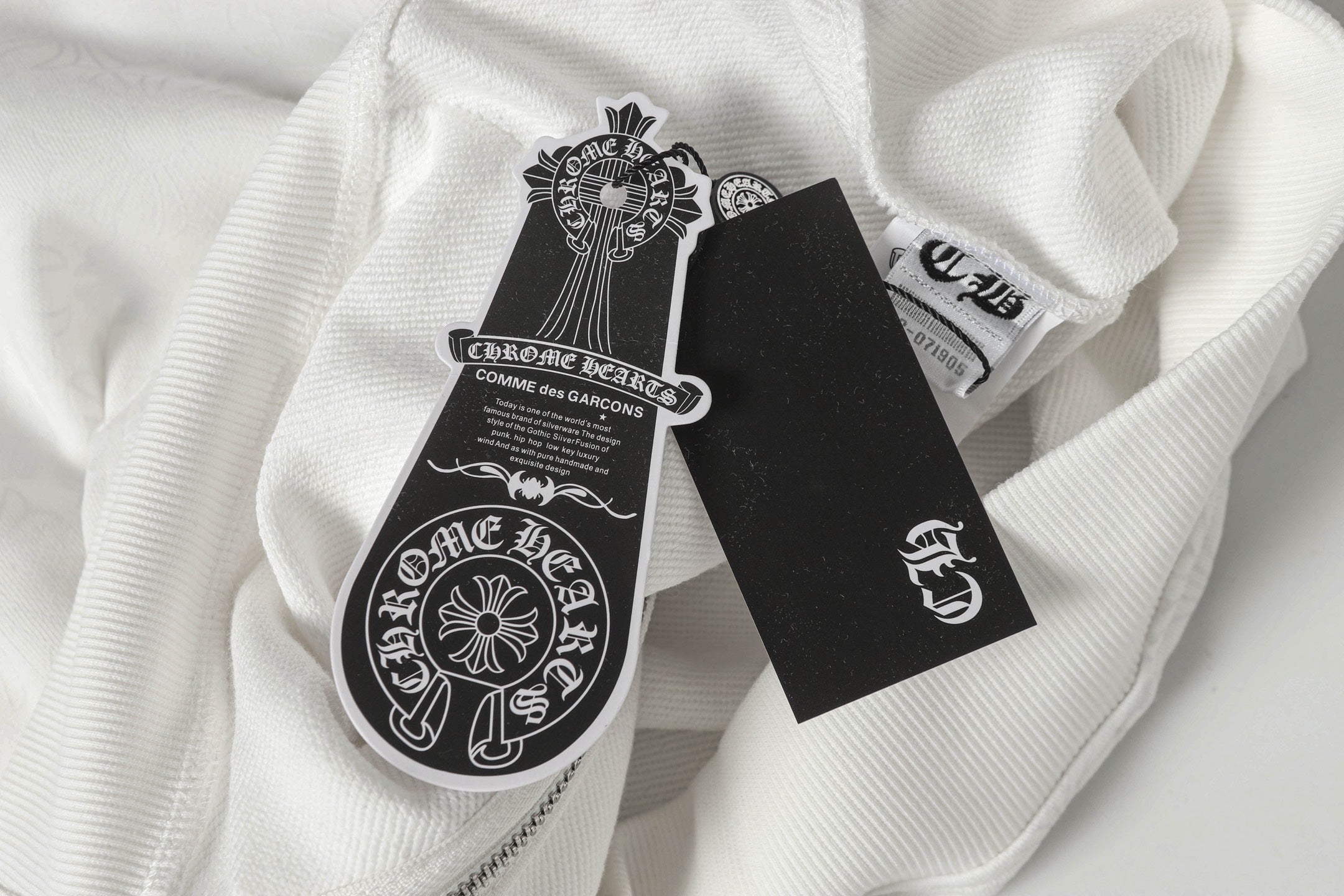 White zip-up hoodie with printed sleeve crest patch and black care tag