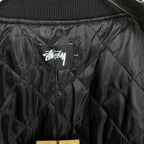 Black quilted bomber jacket interior with Stussy logo label and buttons