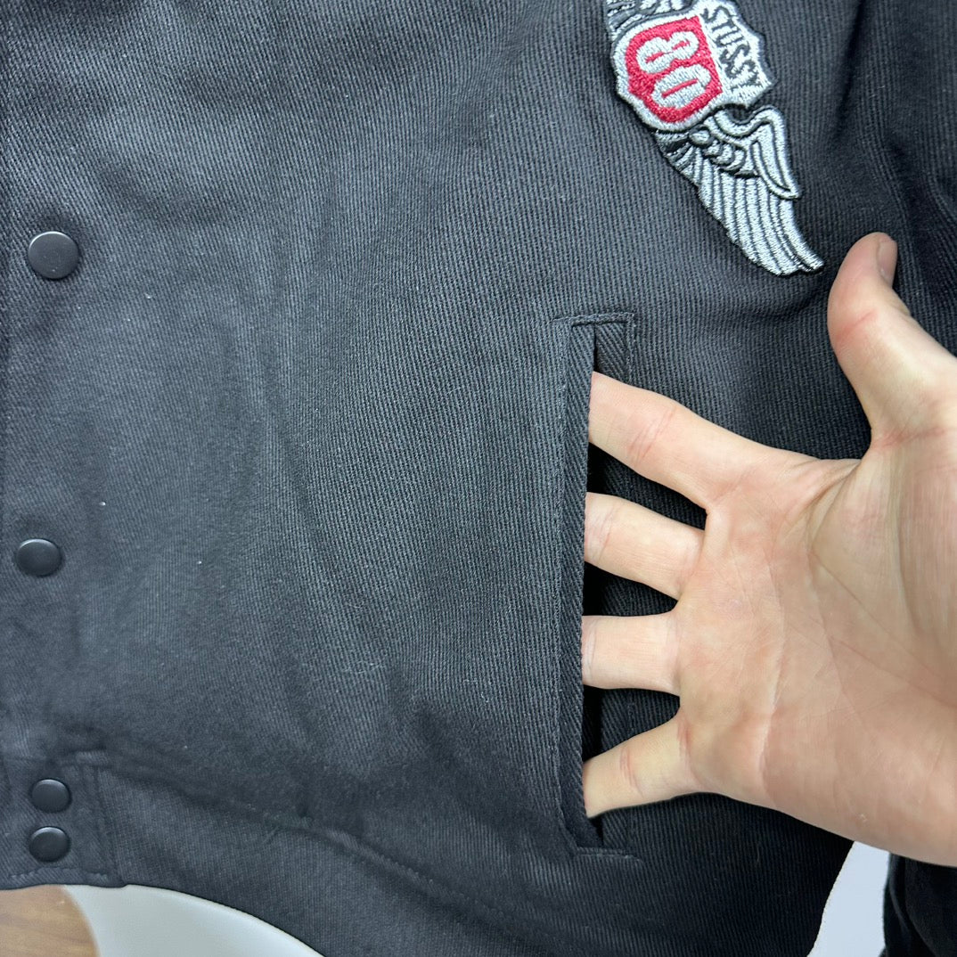 Black bomber jacket sleeve cuff with embroidered patch detail near shoulder