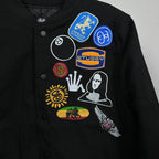 Black Stussy bomber jacket close-up with colorful round and portrait patches