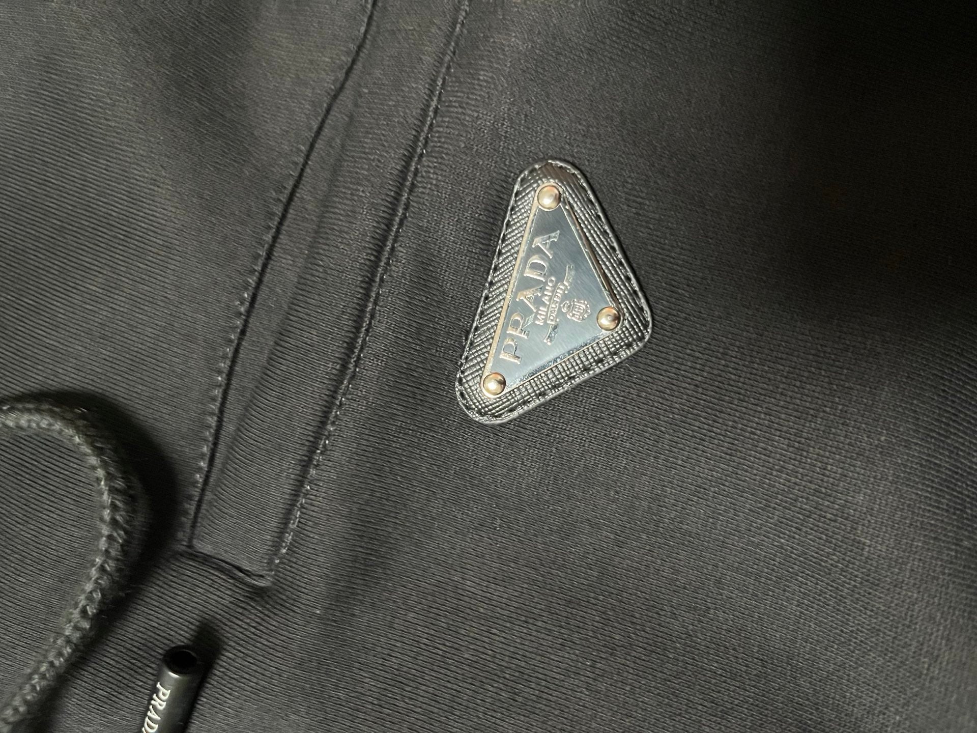 Triangular Prada logo patch on dark hoodie fabric