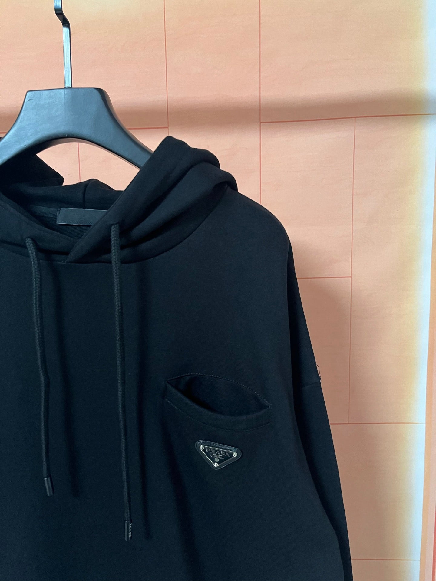 Dark hoodie with chest pocket and small triangular logo patch