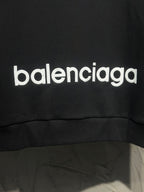 Black hoodie with large white Balenciaga logo print near hem.