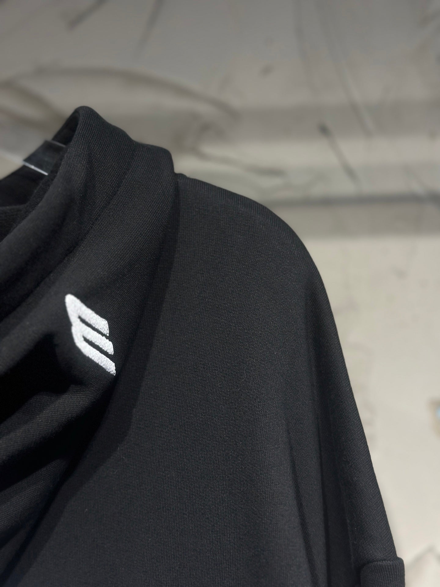 Black hoodie sleeve with small white Balenciaga logo on shoulder.