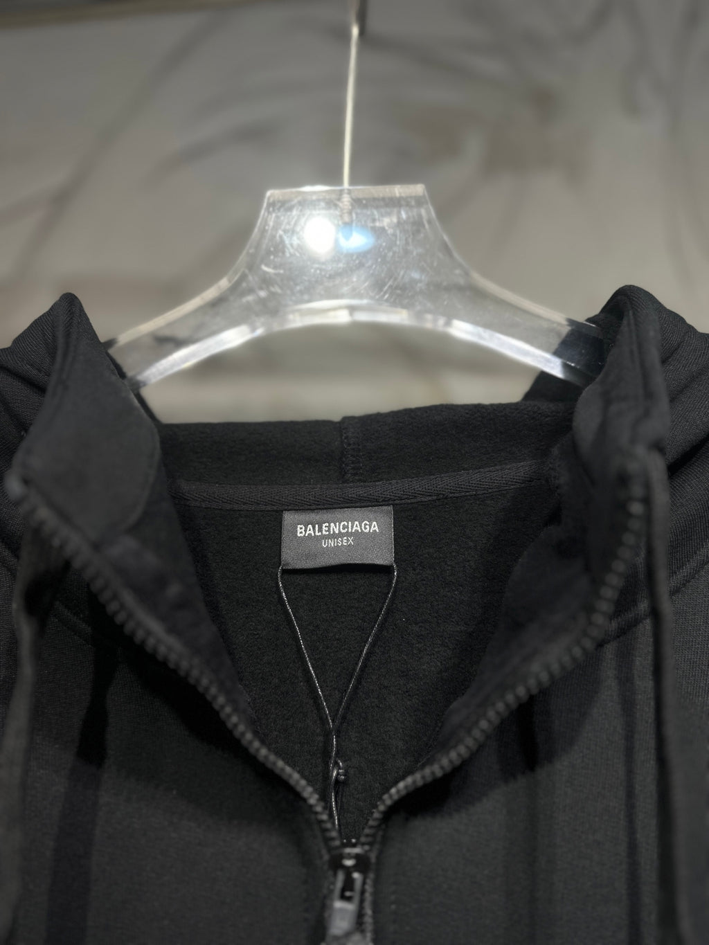 Black zip-up hoodie with hood and front zipper, shown with brand tag.