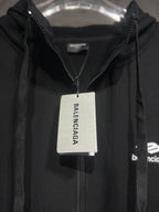 Black Balenciaga hoodie with zip front and hood, hanging with brand tag.