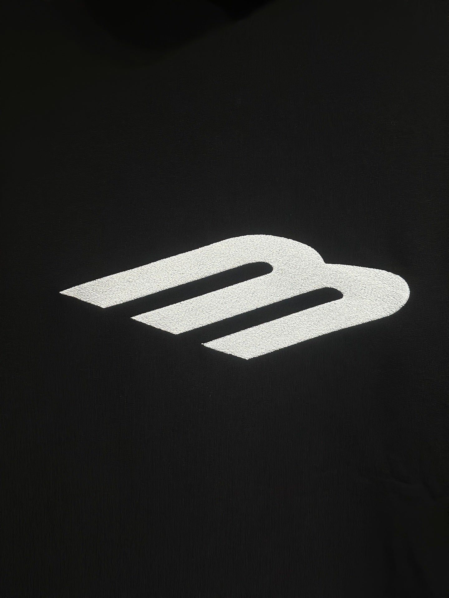 White Balenciaga icon logo on black hoodie fabric.