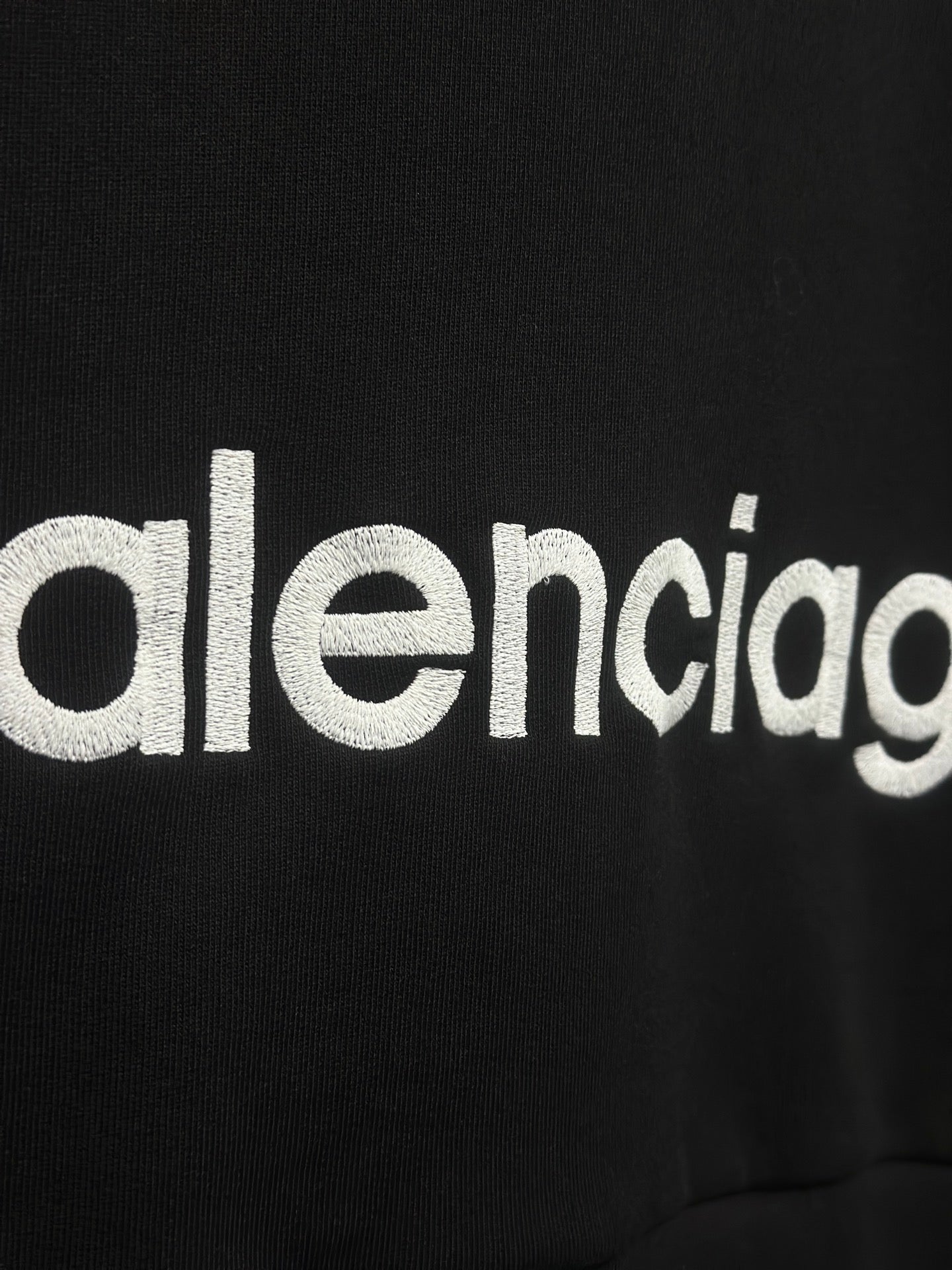 White Balenciaga wordmark on black hoodie fabric.