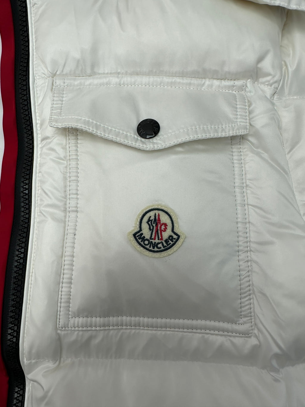 White puffer jacket chest pocket with black button and Moncler emblem