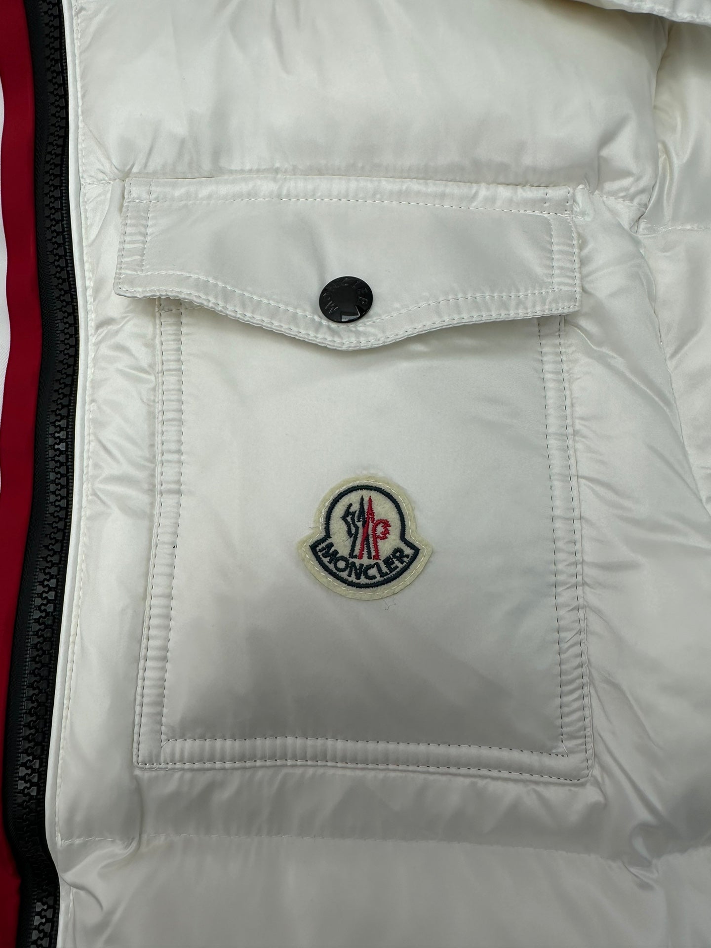 White puffer jacket chest pocket with black button and Moncler emblem