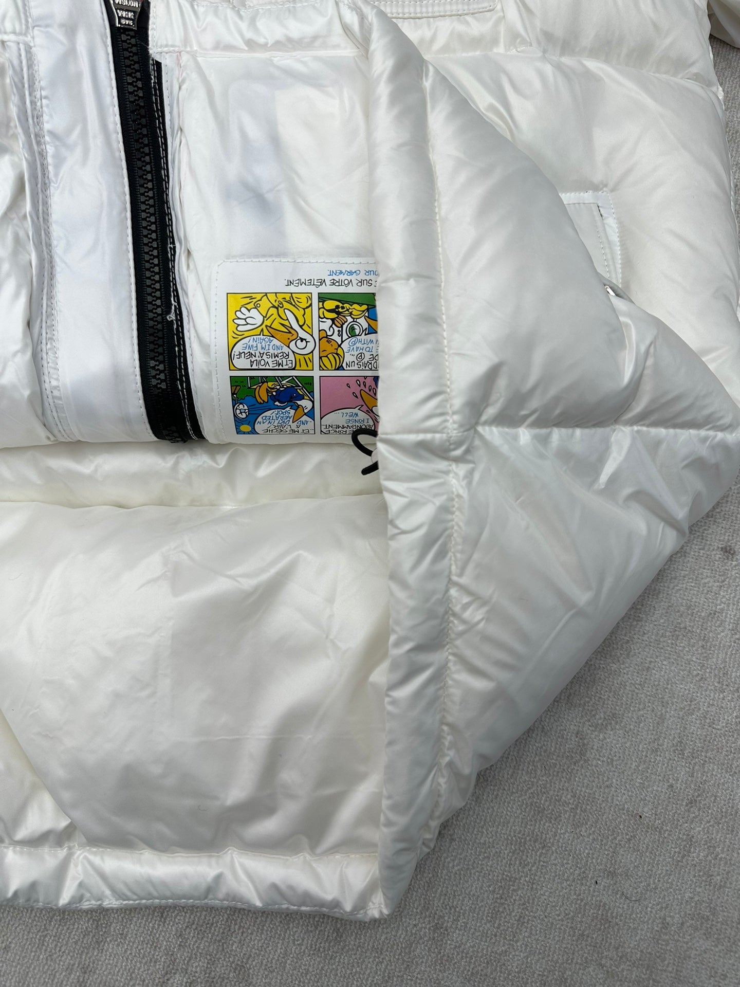 White puffer jacket with interior care label patch and black zip edge