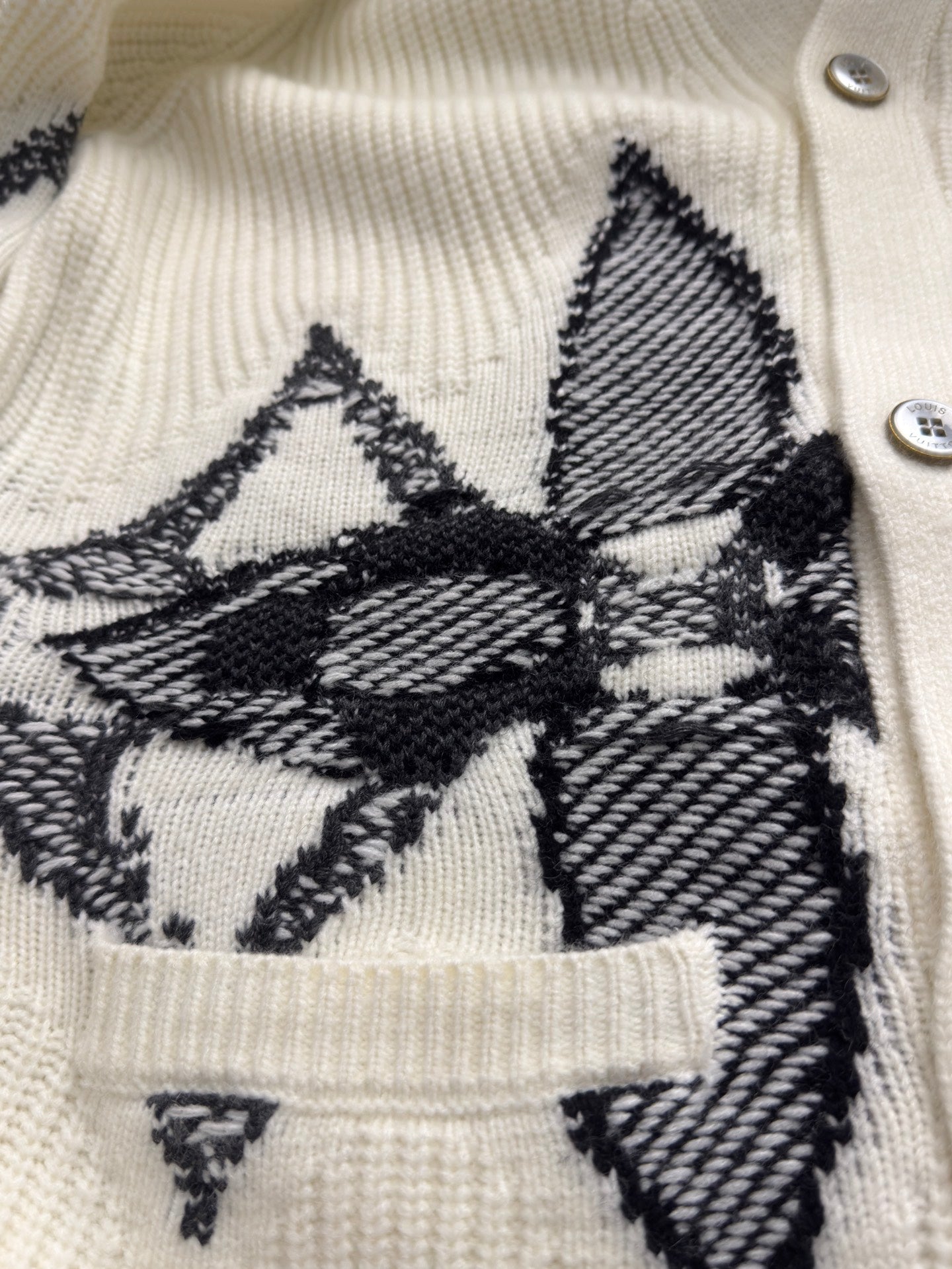 Cream knit cardigan front with black star-and-floral graphic and buttoned placket