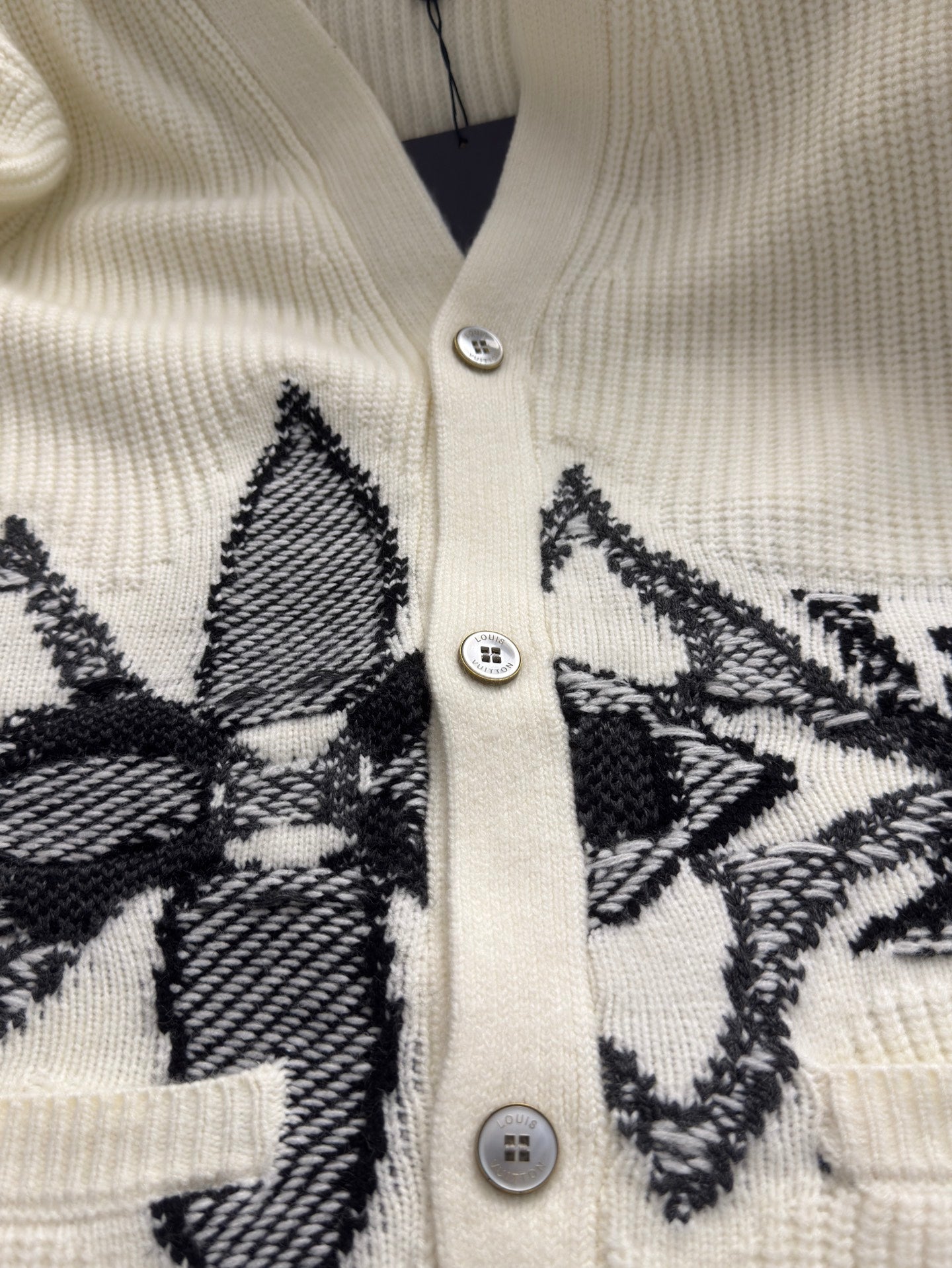 Cream rib-knit cardigan front with silver button placket and black embroidered pattern