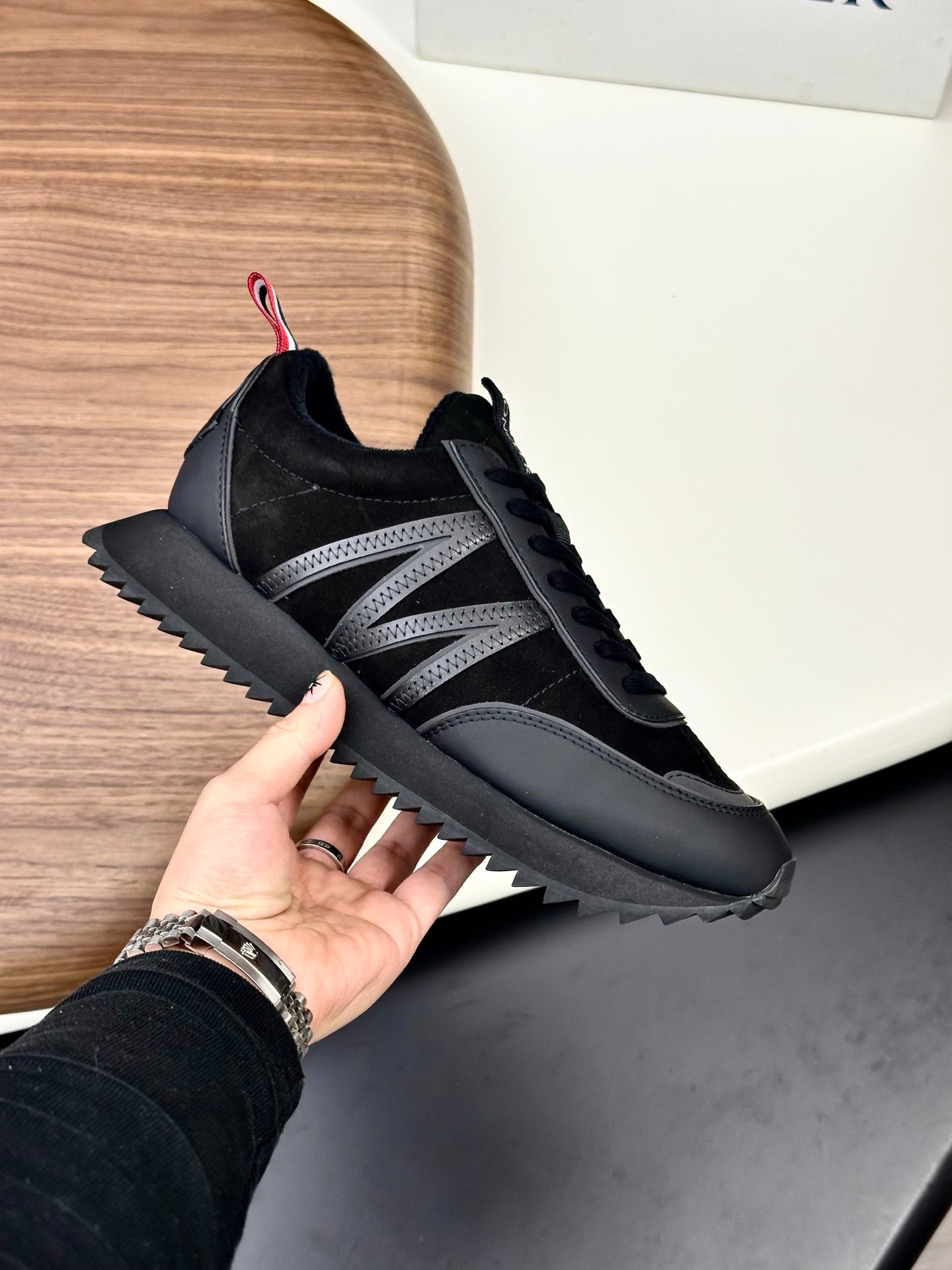 Moncler black sneakers held in hand, lace-up with gray panel detailing