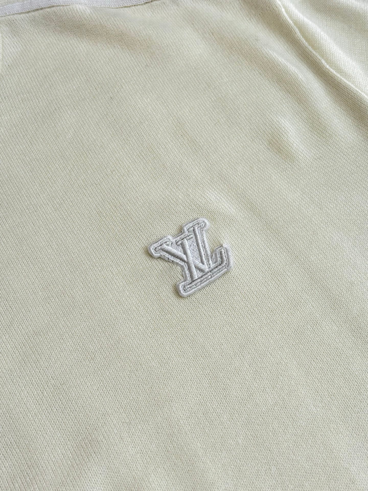 Cream sweater front with raised embroidered LV-style emblem near chest