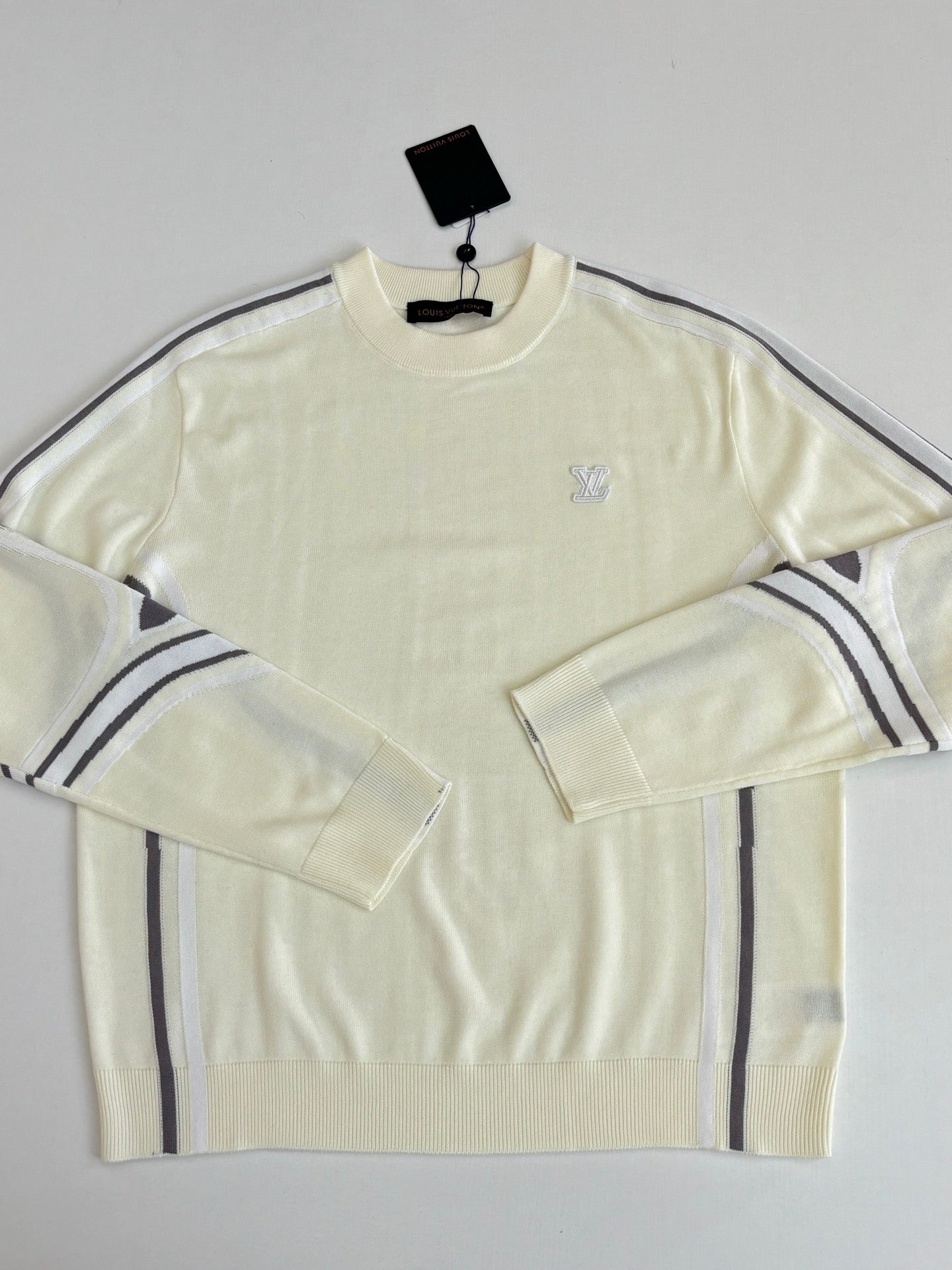 Cream long-sleeve sweater with small chest logo and navy-striped shoulder panels